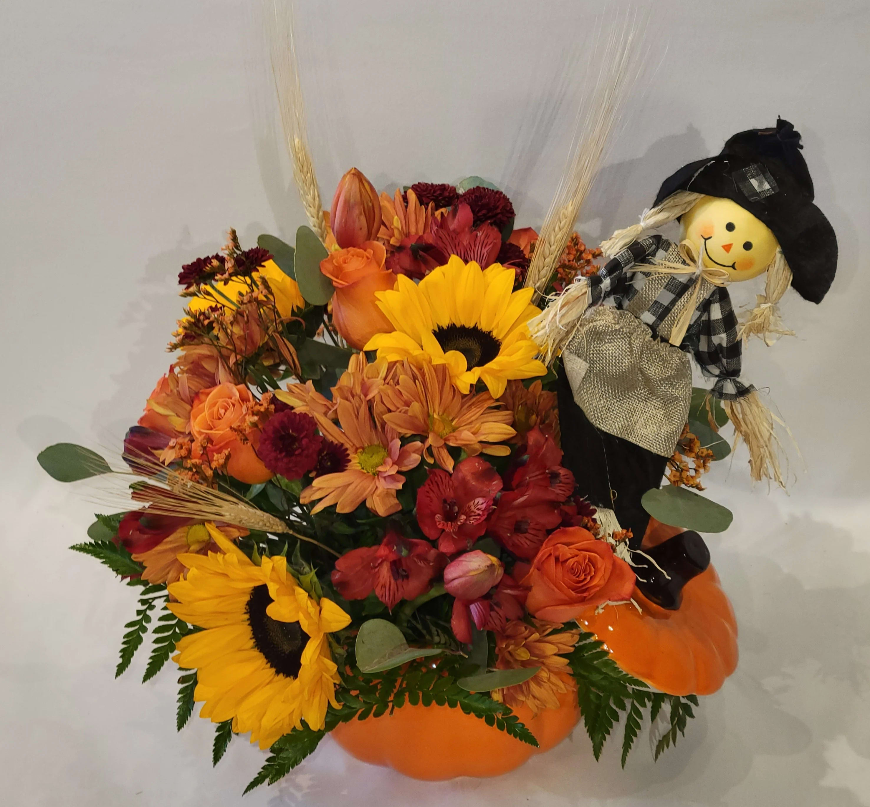 Autumn floral arrangement in a pumpkin container with a scarecrow decoration