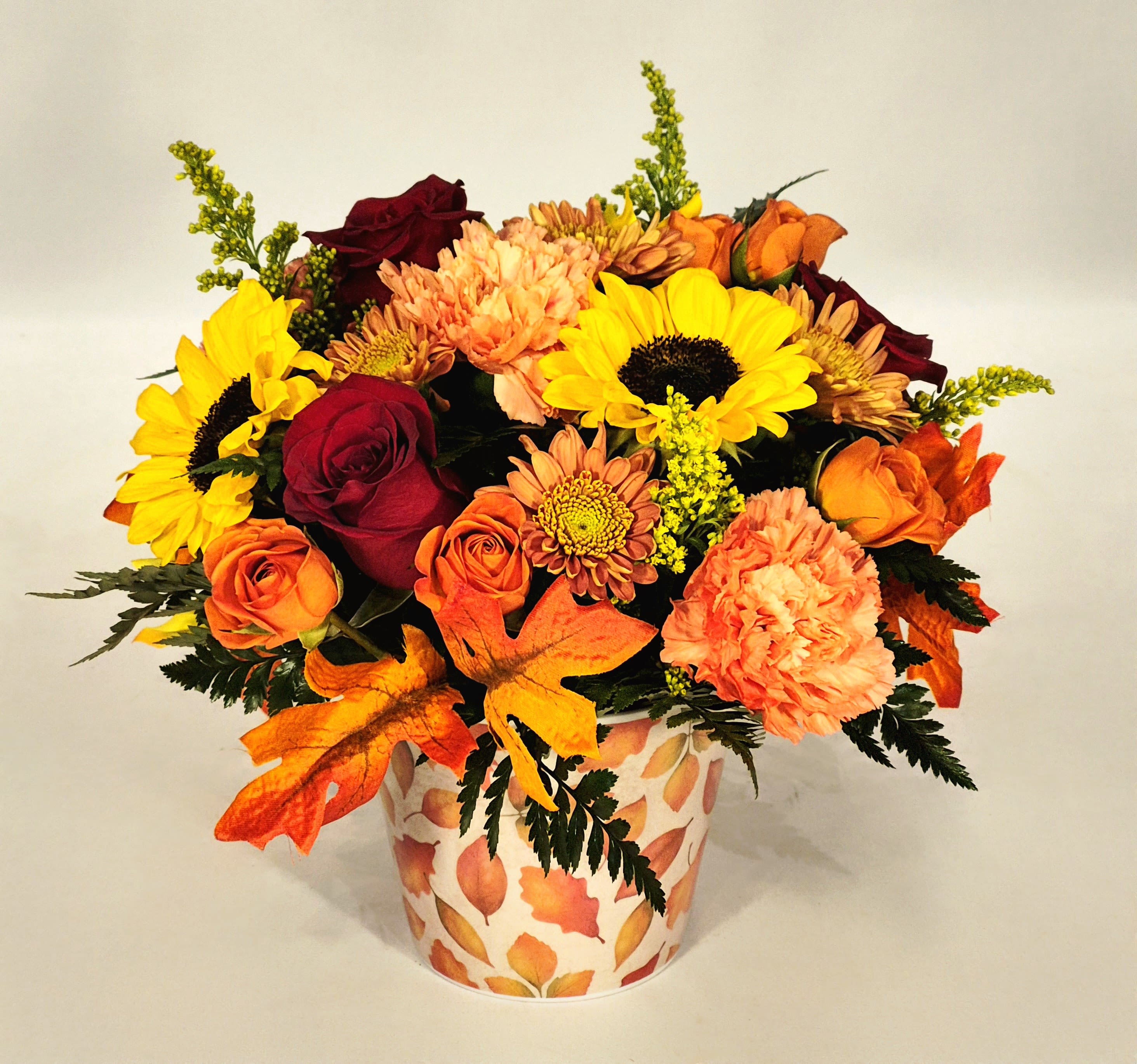 Fall bouquet of sunflowers, roses, and mums in a leaf-patterned vase
