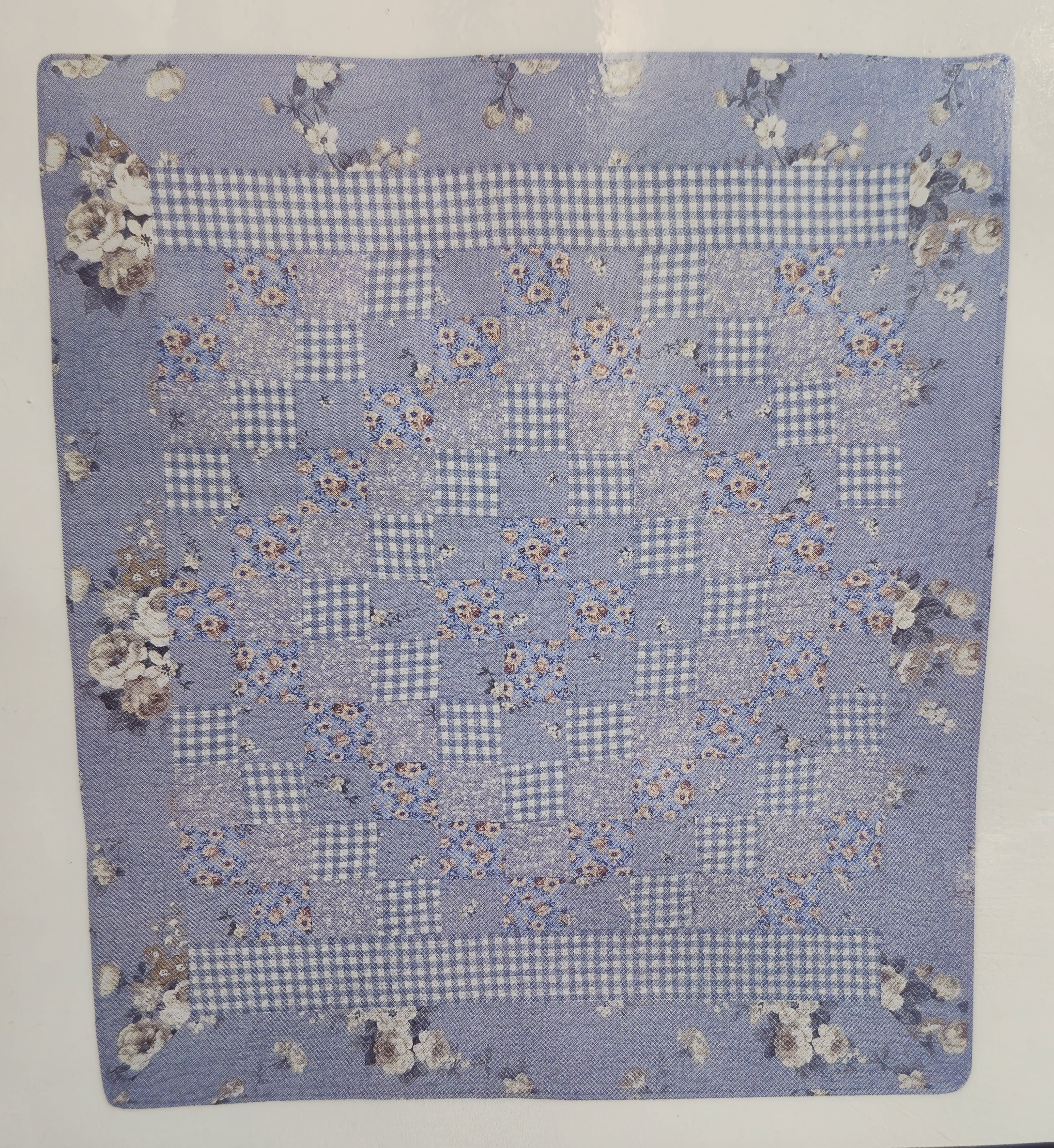 Blue and White Diamond Pattern Quilt - The soft, patchwork quilt in soothing blue, white and lavender tones offers a comforting presence for sympathy, funeral or get-well gestures - the kind of textile that quietly says you're thinking of someone. As a funeral or memorial accent or a bedside comfort for someone recovering at home, this Blue and White Diamond Pattern Quilt reads as gentle and nostalgic, a thoughtful alternative or addition to floral tributes for Grandparent's Day or Mother's Day when you want to wrap a loved one in warmth.  Hand-quilted look with gingham checks, small floral prints and scattered blossom motifs around the border, the 50 x 60 throw folds neatly for presentation and arrives finished with a bow when sent on its own. The sale can include the simple wire easel stand (tall triangular frame with a horizontal support) for an additional charge when you prefer a formal display at a service or memorial; choose the Deluxe option to add the easel for presentation.