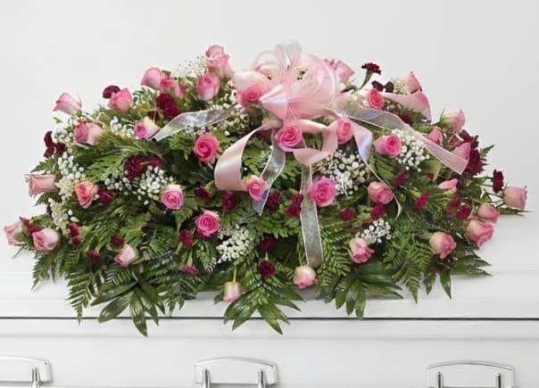 Pink rose casket spray with ribbon on a white casket