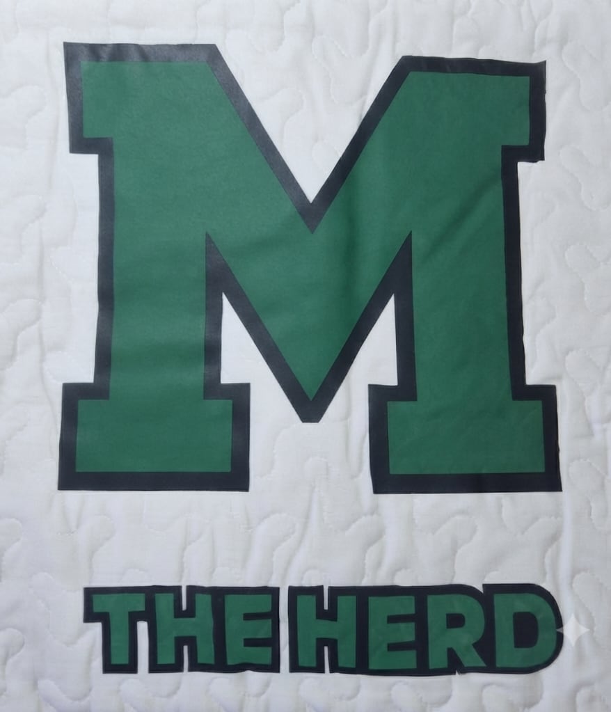 Green letter M with the words THE HERD on a white quilted background