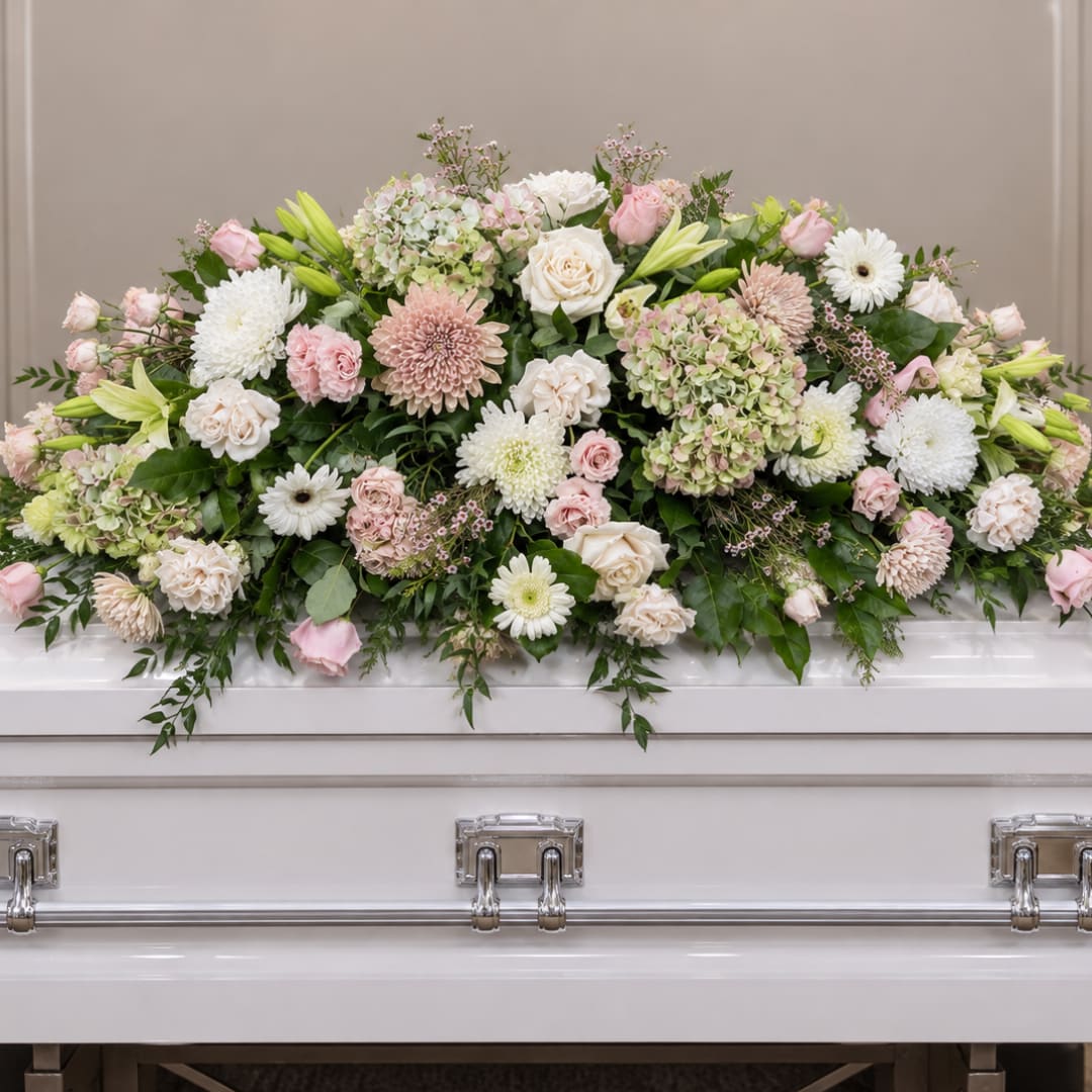 Pastel floral casket spray with roses, lilies, and white daisies