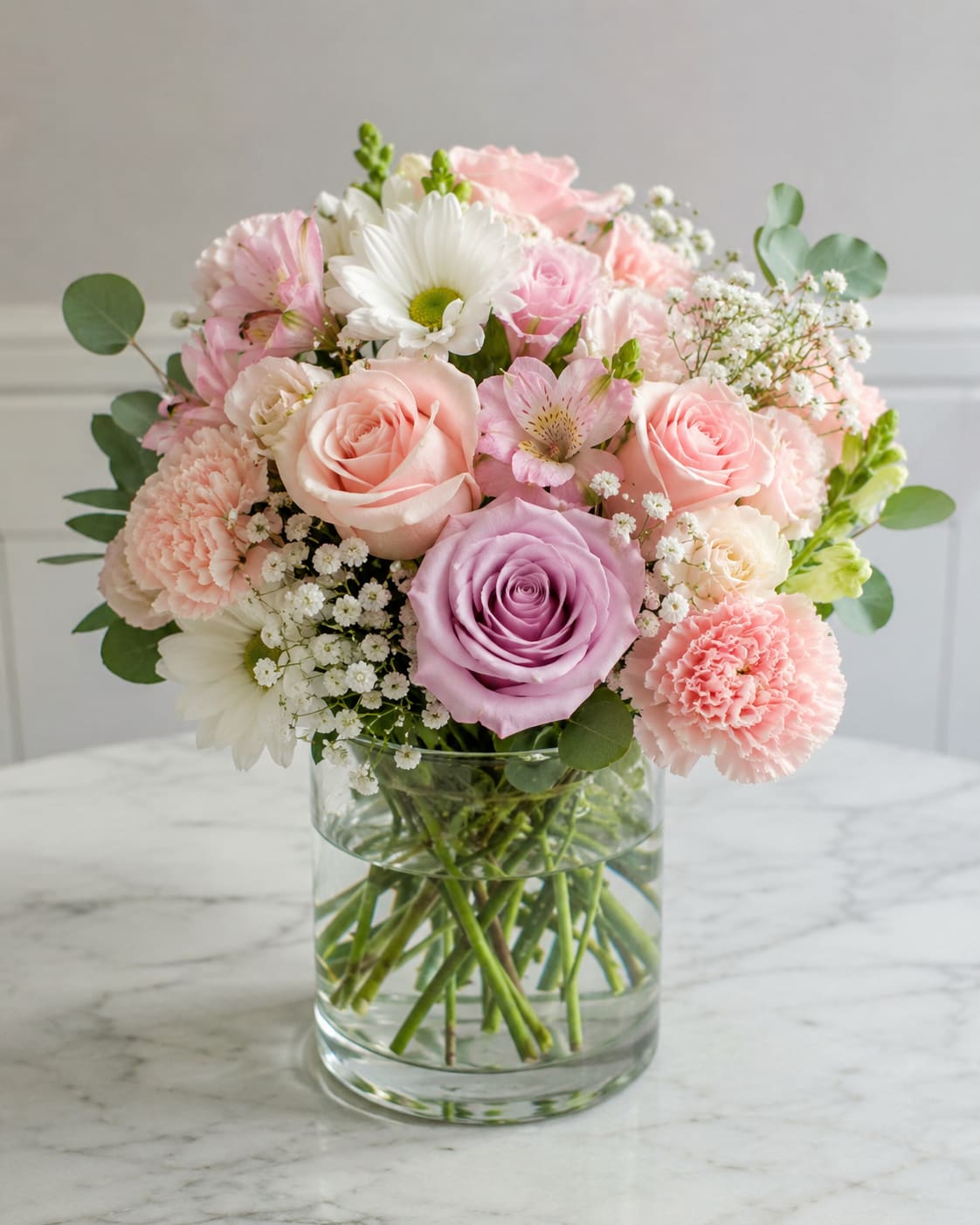 Perfectly Pretty by Petal Perfection Flower Company  - Soft pink roses and lavender accents form a rounded, airy bouquet that reads as gentle and romantic-perfect for a birthday bouquet, anniversary flowers, or a spring celebration. The soft palette of pink, white, purple, and green creates a fresh, feminine look that lets the recipient feel warmly celebrated the moment they see it.  This arrangement pairs roses, carnations, daisy-like blooms, alstroemeria, and touches of baby's breath with eucalyptus for a light, natural frame, all gathered in a clear glass vase. The compact, rounded presentation suits tabletops and bedside tables and feels both cheerful and elegant without overwhelming a room.  Send this as a thoughtful everyday gift or to mark a special milestone; the mix of textures-from velvety roses to delicate alstroemeria-makes the recipient feel truly seen. Arrives ready to display in its clear glass vase; swap the water and trim stems every few days to keep blooms fresh longer.
