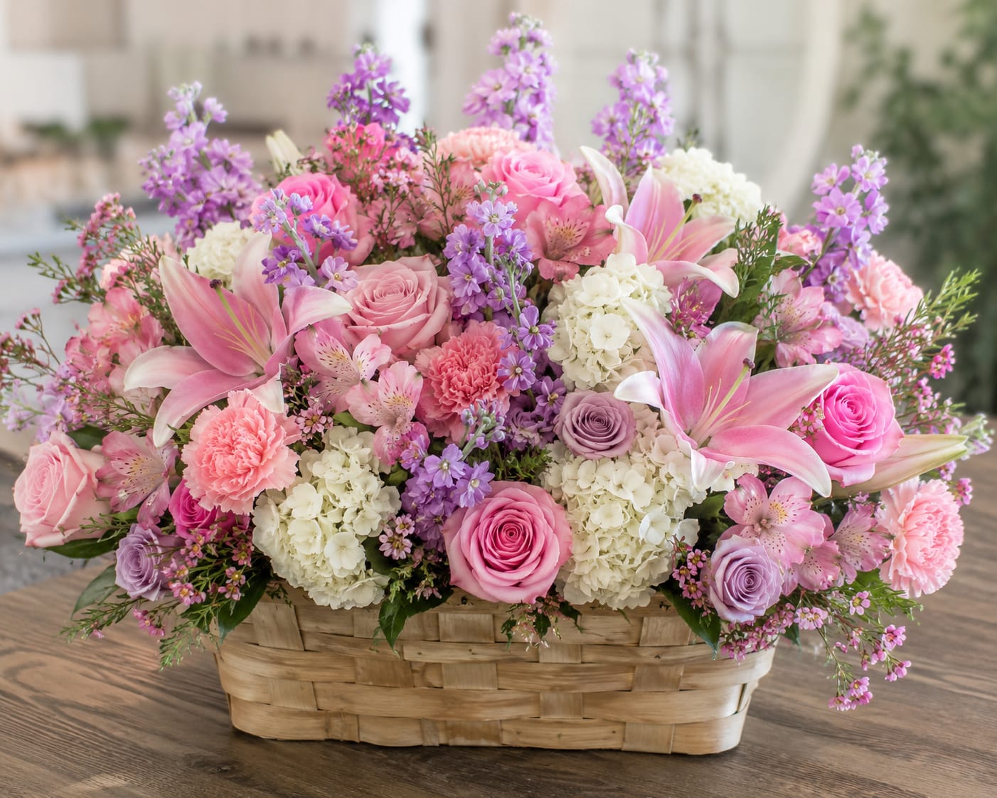 Hearts Garden  - A lush, garden-style basket overflowing with soft pink roses and lilies sets a romantic, cheerful tone-perfect as a birthday bouquet, anniversary gift, or just-because surprise for someone you adore. The low, full design reads warm and affectionate so the recipient feels truly celebrated the moment it arrives.  This full, low woven basket is packed with pink roses, pink lilies, white hydrangeas, carnations, alstroemeria, and small purple accent blooms for a mix of pink, lavender, and white hues. The varied textures-from fluffy hydrangea heads to the sculpted rose petals and starry alstroemeria-create depth and a hand-gathered garden look that sits beautifully on a table or mantel.  Ideal for sending congratulations, saying "I'm thinking of you," or marking a romantic milestone, the arrangement arrives ready to display in its giftable basket. For best enjoyment, keep flowers in a cool spot away from direct sun and refresh the water as needed to prolong blooms.