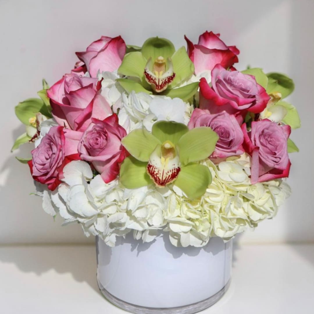 Pink roses and green orchids arranged with white hydrangeas in a white vase