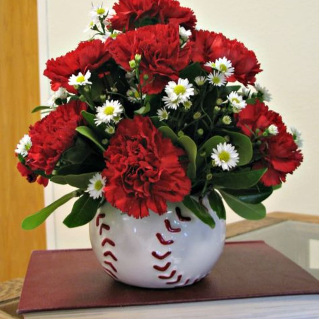 Red carnations and white daisies in a baseball-shaped vase