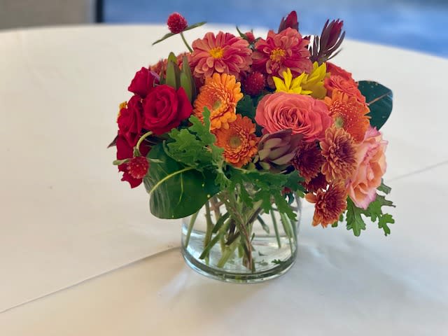 Mixed bouquet of red, orange, and pink flowers in a clear glass vase