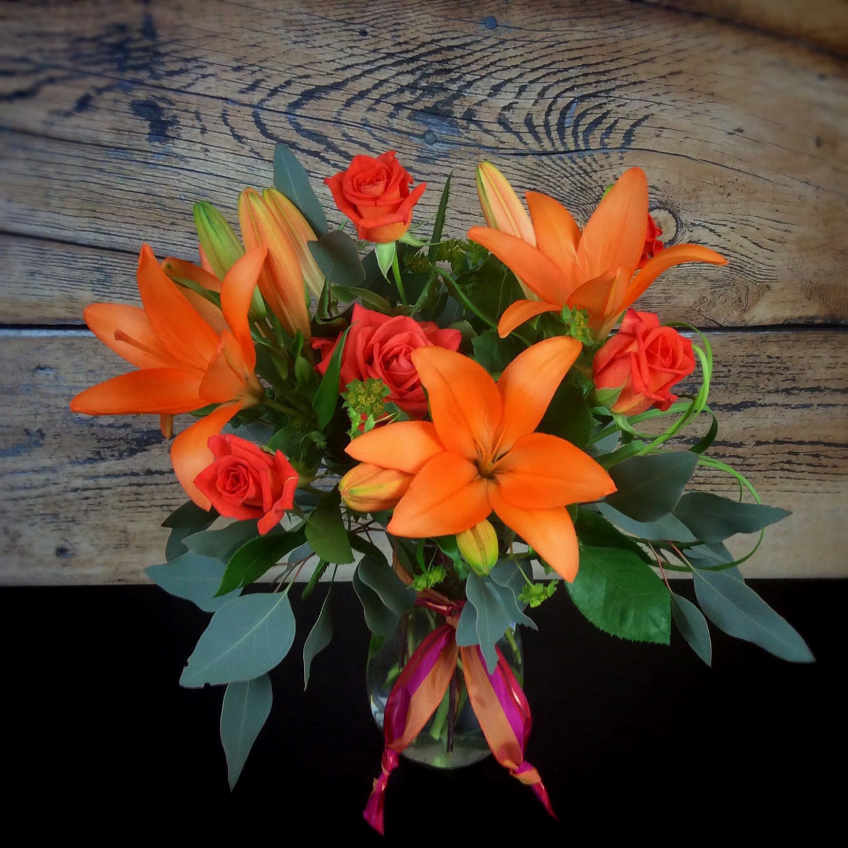 Orange lilies and red roses in a glass vase with a ribbon