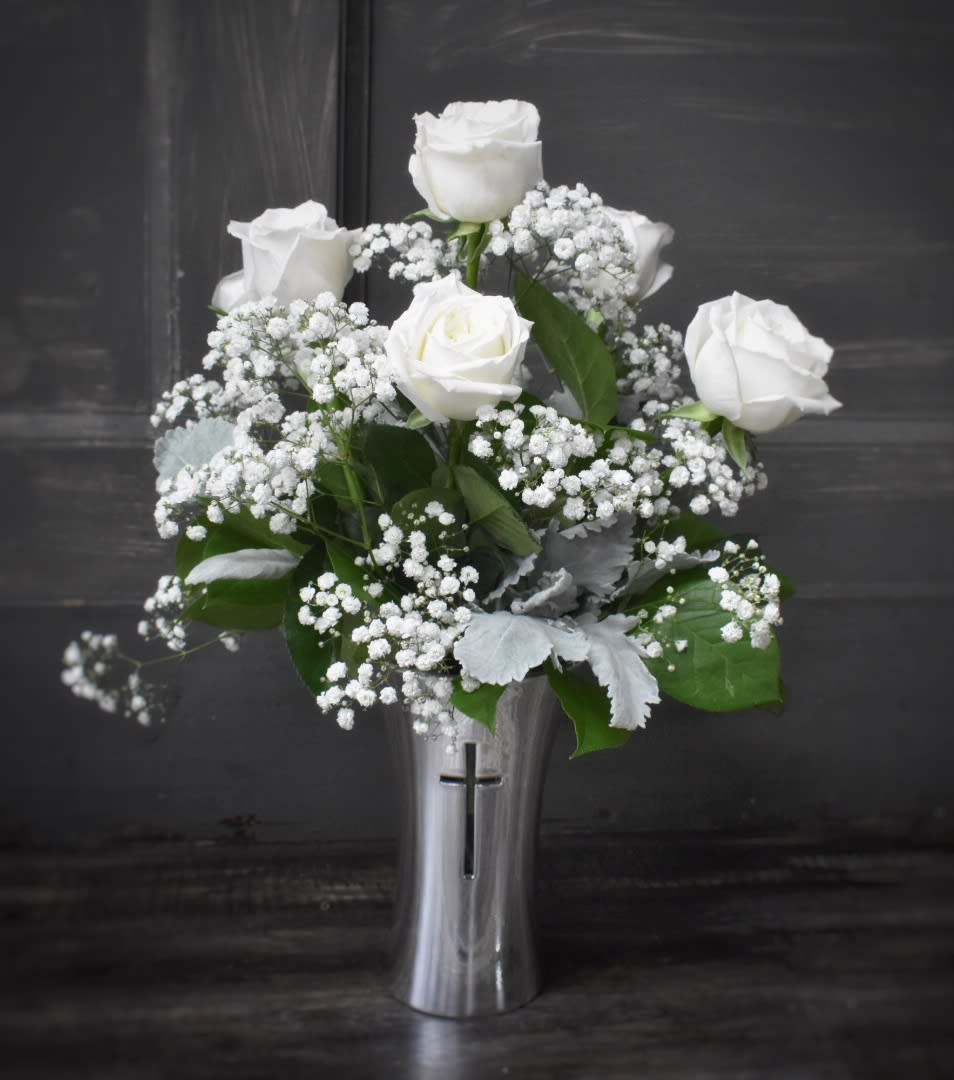 White roses and baby's breath in a silver vase with a cross