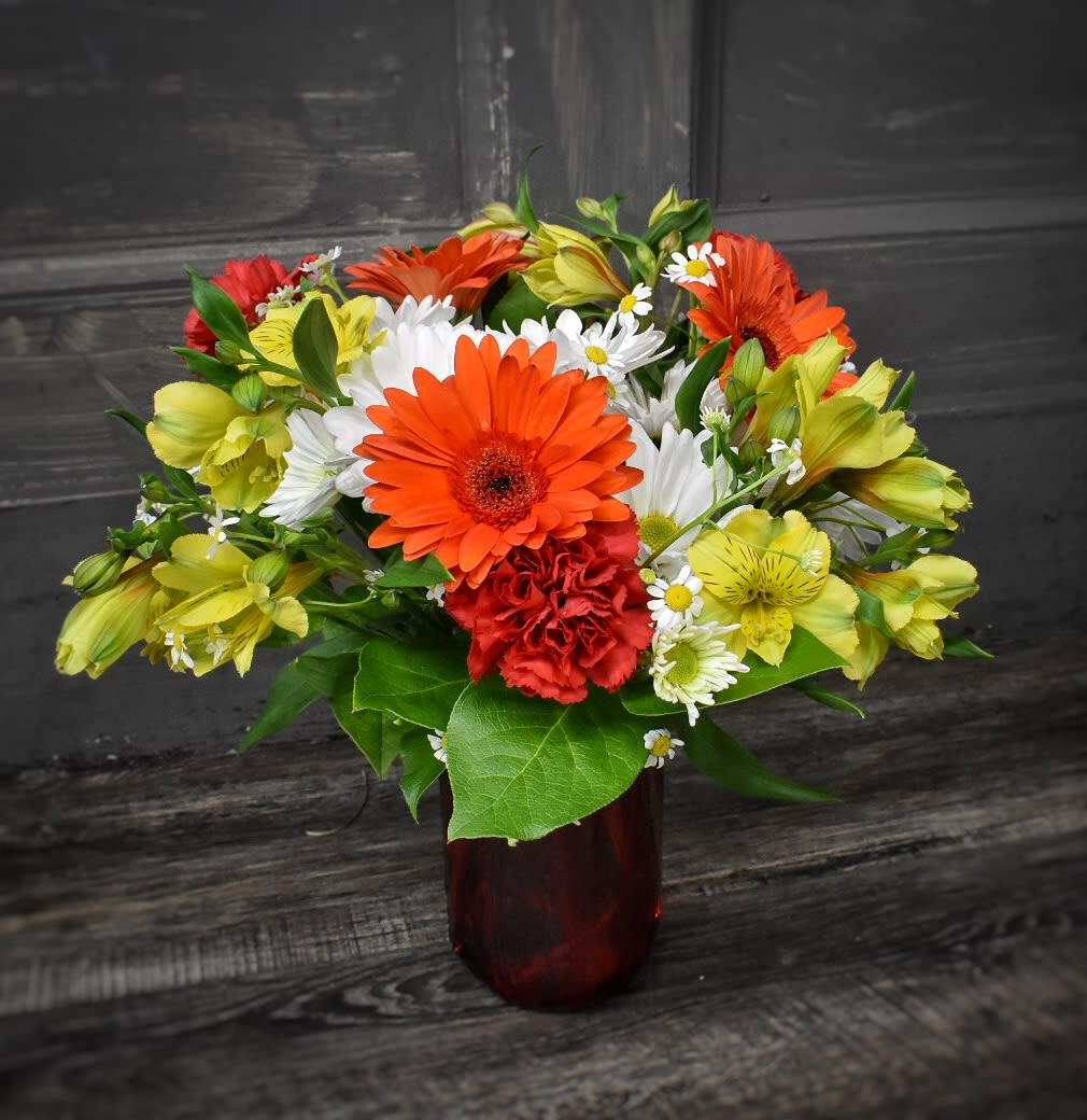Mixed bouquet of orange, yellow, white, and red flowers in a red vase