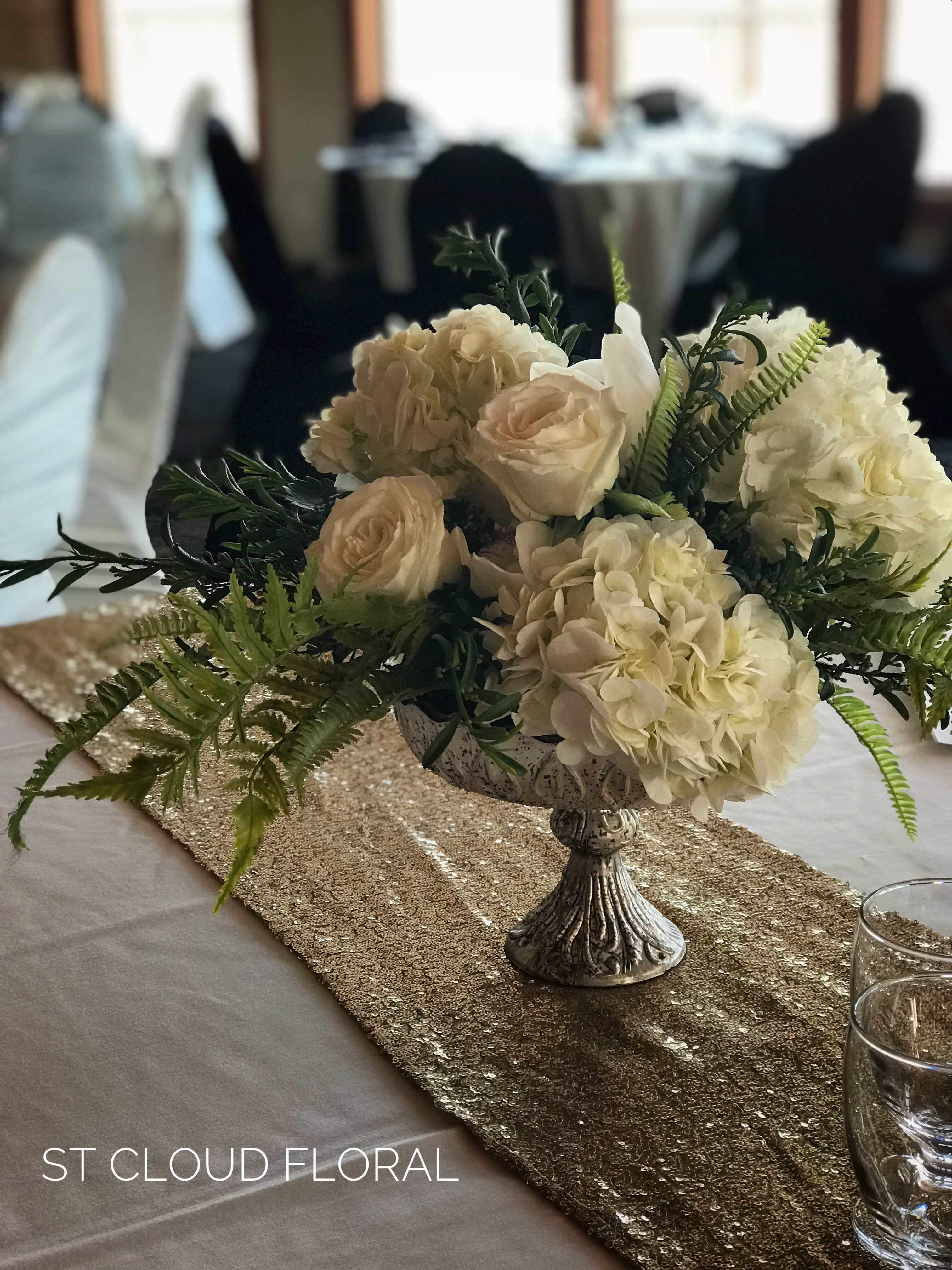 Cream floral centerpiece in a silver pedestal bowl on a table runner