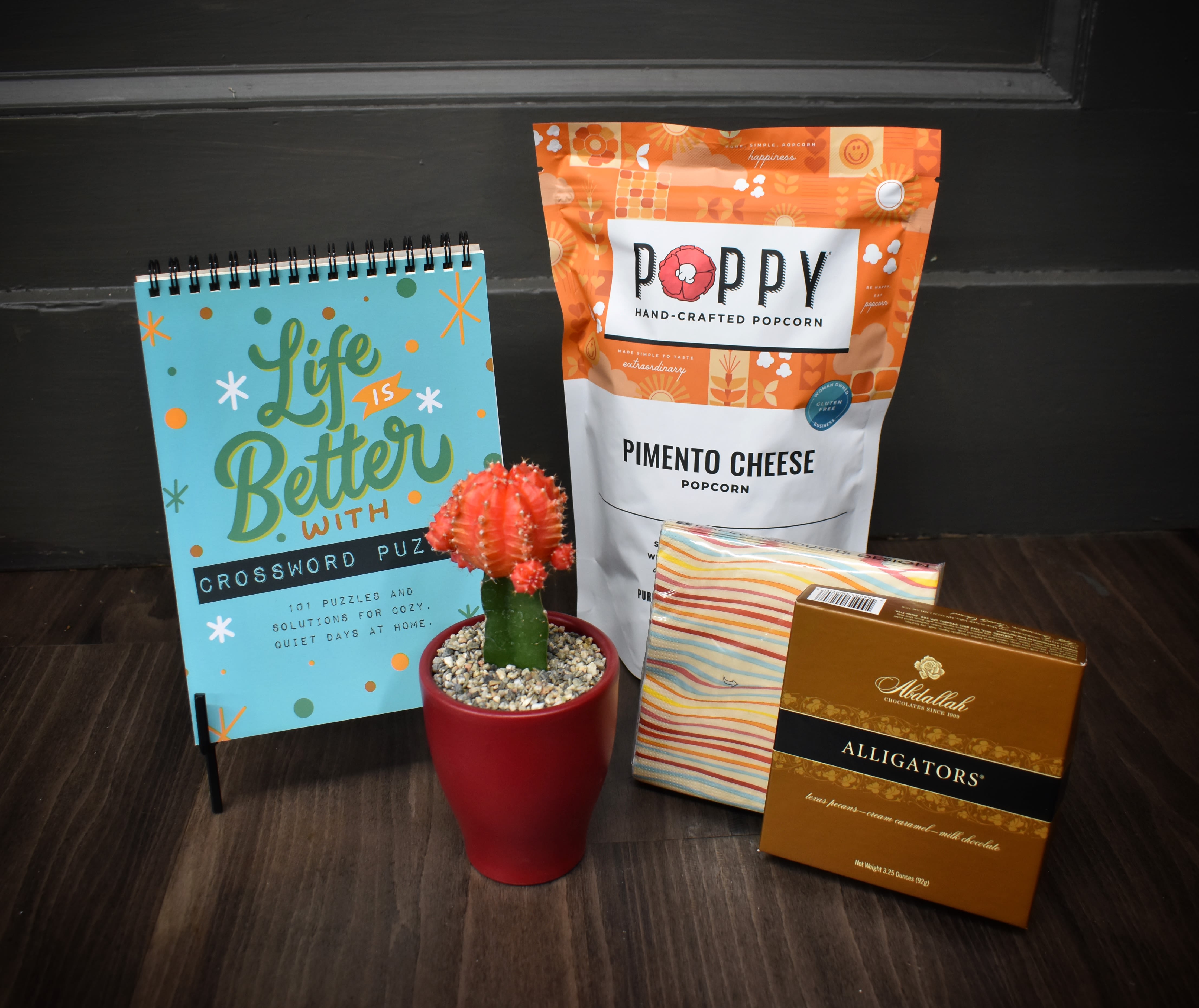Gift set with a potted cactus, crossword notebook, popcorn, napkins, and chocolates