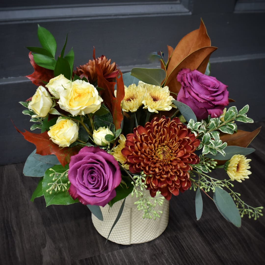 Mixed bouquet of purple and yellow roses with chrysanthemums in a white vase