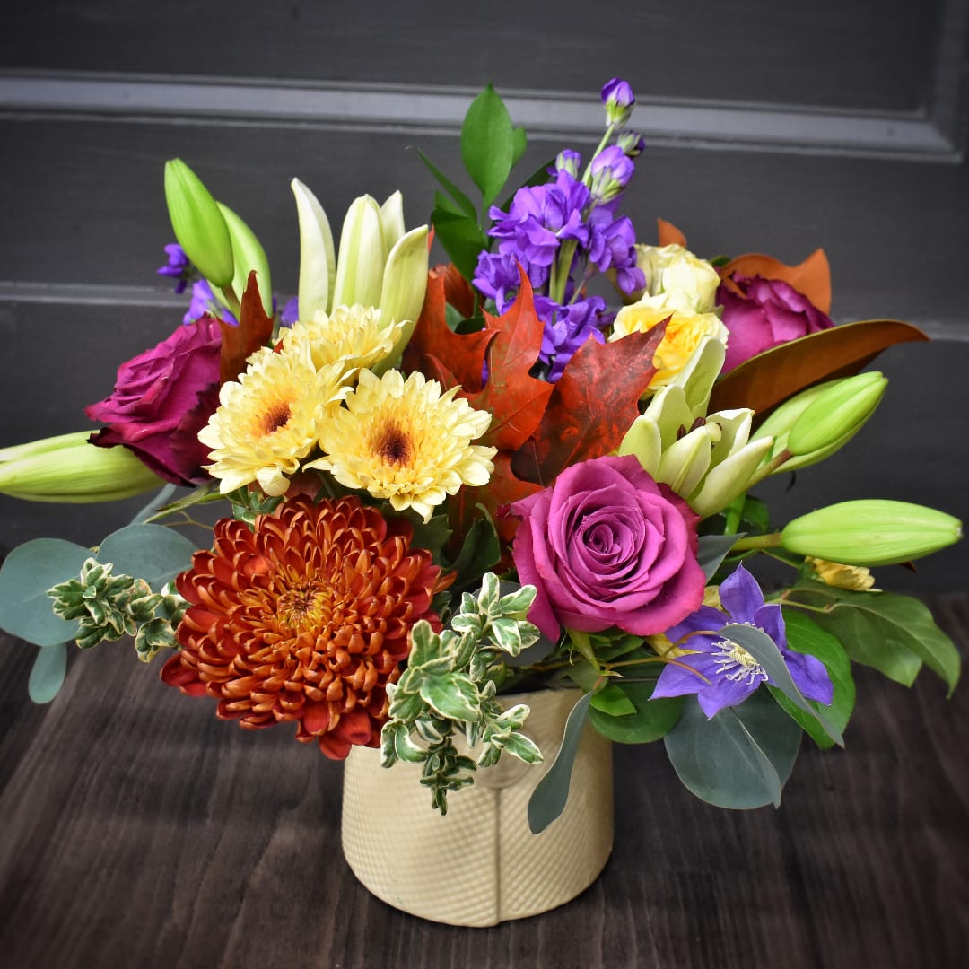 Mixed bouquet in a cream vase with purple, yellow, and orange blooms