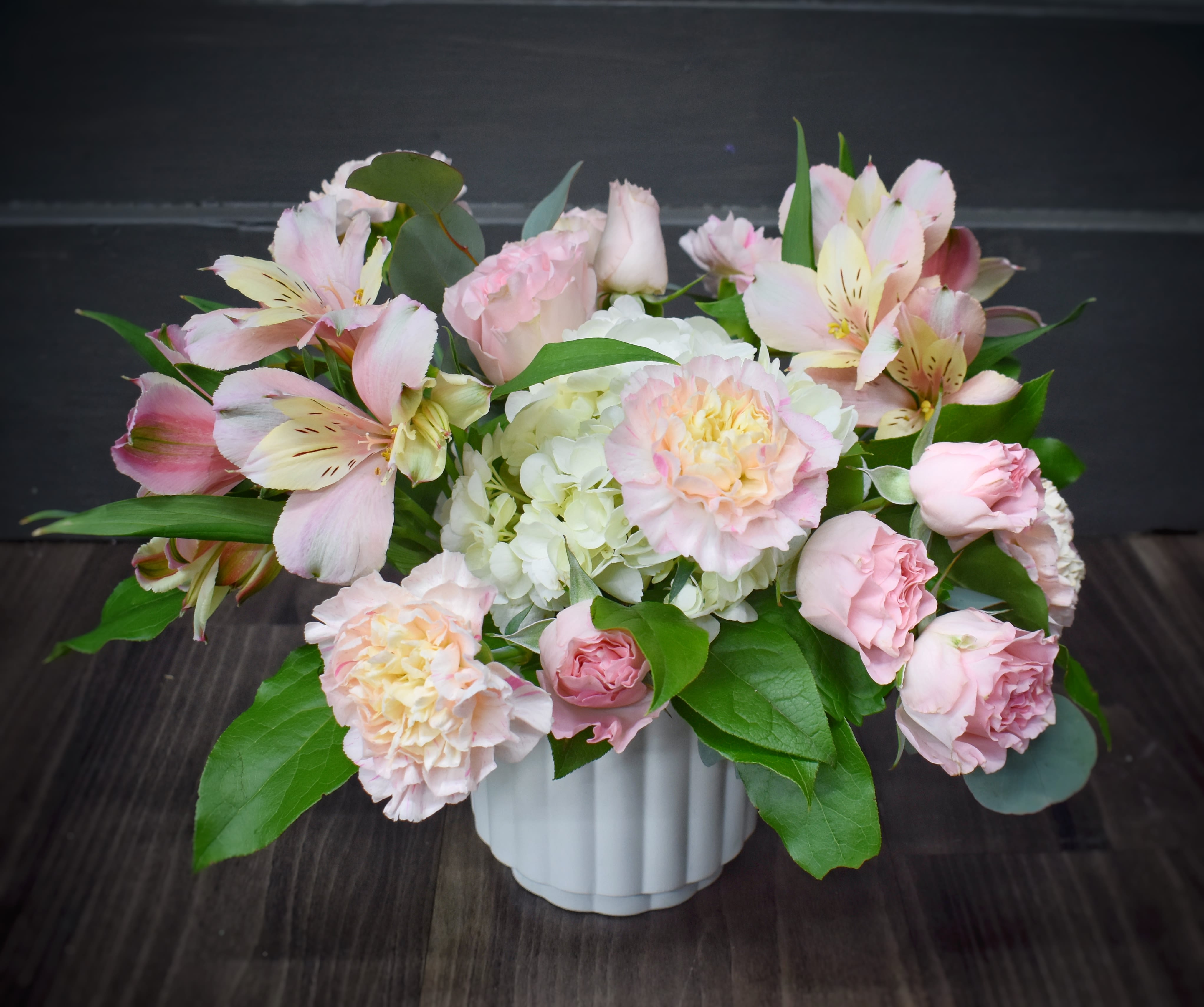 Cotton Candy Pink - A soft, romantic centerpiece of pink and white blooms that reads like cotton candy in flower form-perfect as a birthday bouquet, or a gentle thinking-of-you gift. This flower arrangement pairs pink alstroemeria, with pale pink spray roses and ruffled carnations to create a warm, feminine impression the recipient will notice the moment it's set on a table.  The composition sits in a low white ceramic vase and layers textures for a garden-fresh look: a central cluster of creamy white hydrangeas, sprays of alstroemeria &amp; glossy green foliage build a full, rounded silhouette.  Designed at a compact, tabletop scale, this arrangement feels polished yet casual-the kind of gift that makes someone feel truly seen on birthdays, Mother's Day, or as a thoughtful thank-you. The white ceramic vase provides a clean, lasting display; keep blooms in fresh water and out of direct heat to extend their life.