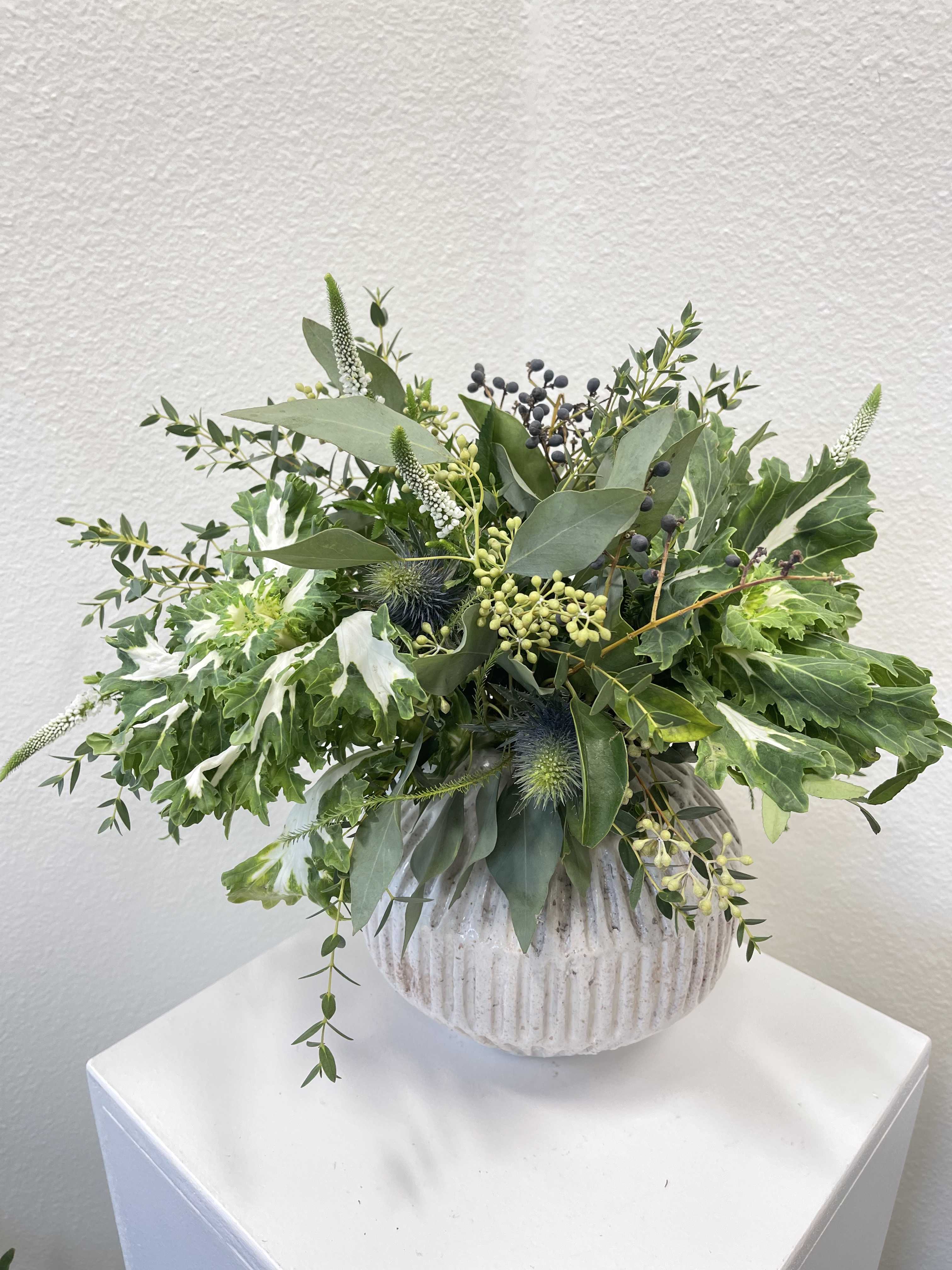Green foliage arrangement in a ribbed white vase