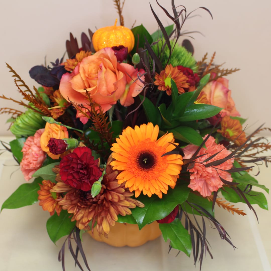 Autumn bouquet in a pumpkin container with orange and red flowers