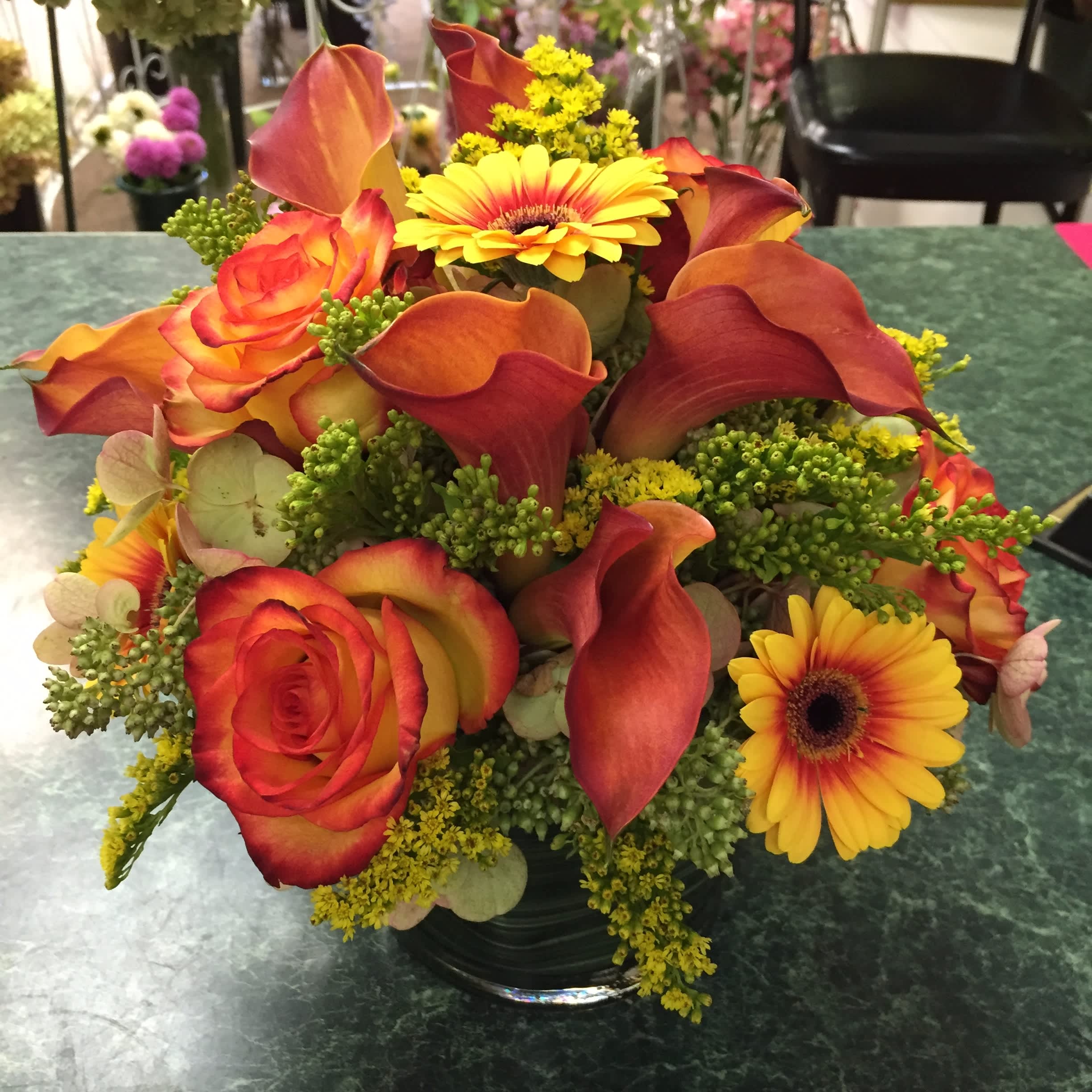 Orange roses, calla lilies, and yellow gerbera daisies in a glass vase