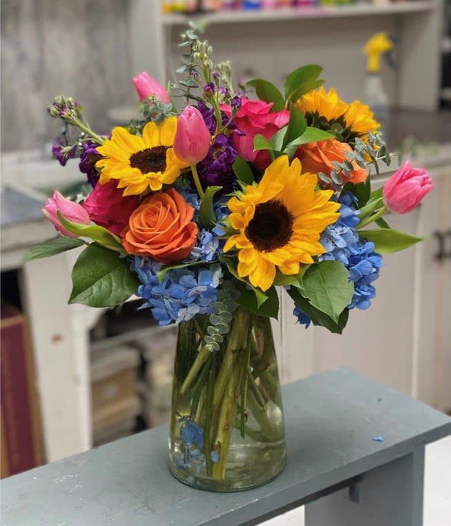 Colorful bouquet of sunflowers, roses, tulips, and hydrangeas in a glass vase