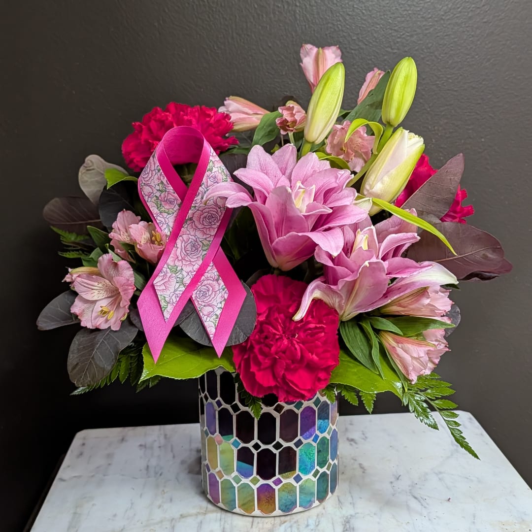Pink lilies and carnations arranged in a mosaic vase with a pink ribbon.