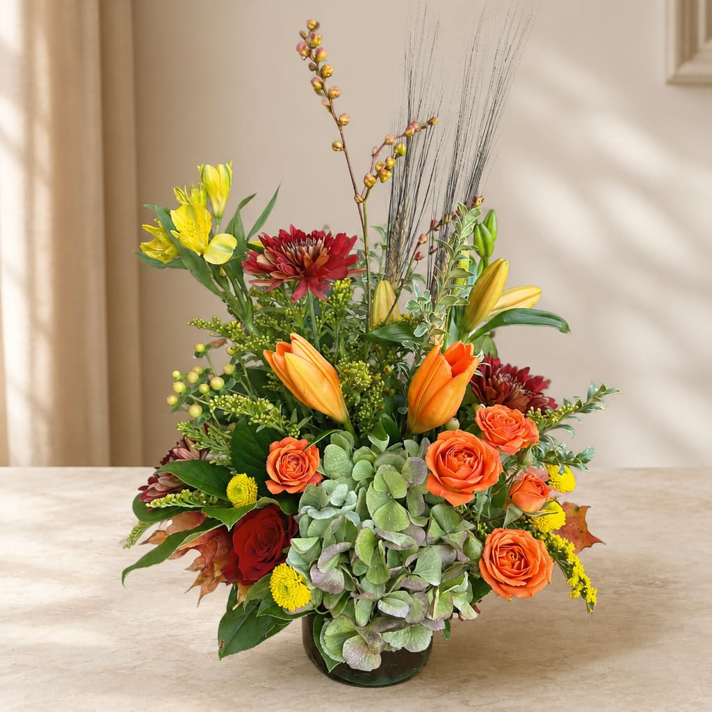 Mixed bouquet in a glass vase with orange roses, lilies, and red blooms
