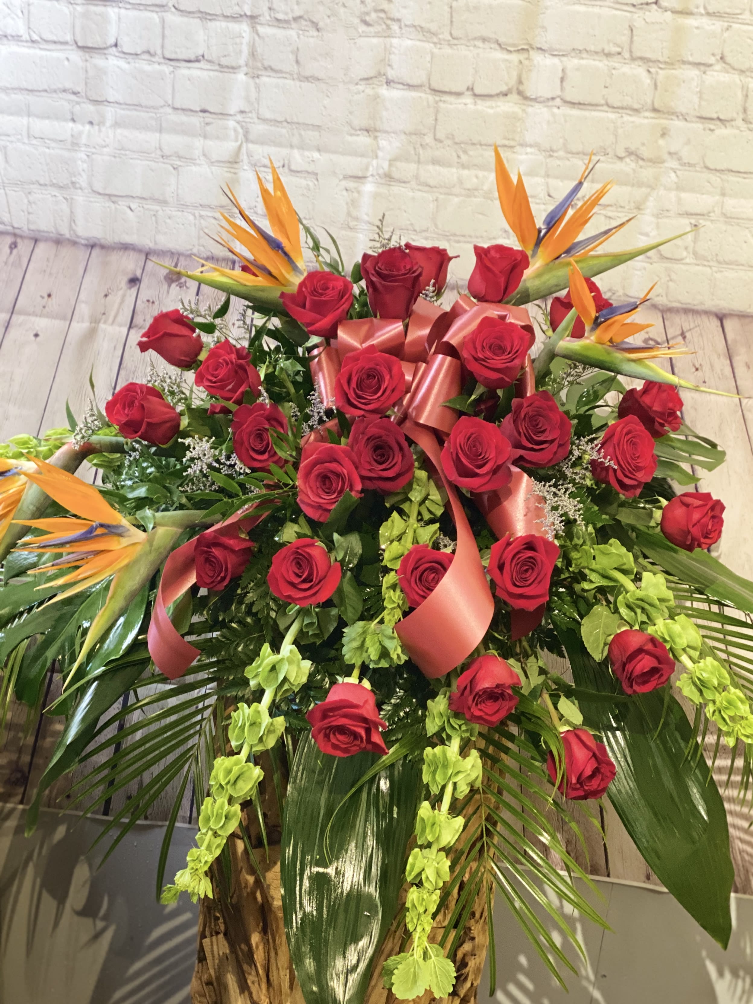 Large bouquet of red roses with orange bird-of-paradise blooms and pink ribbon