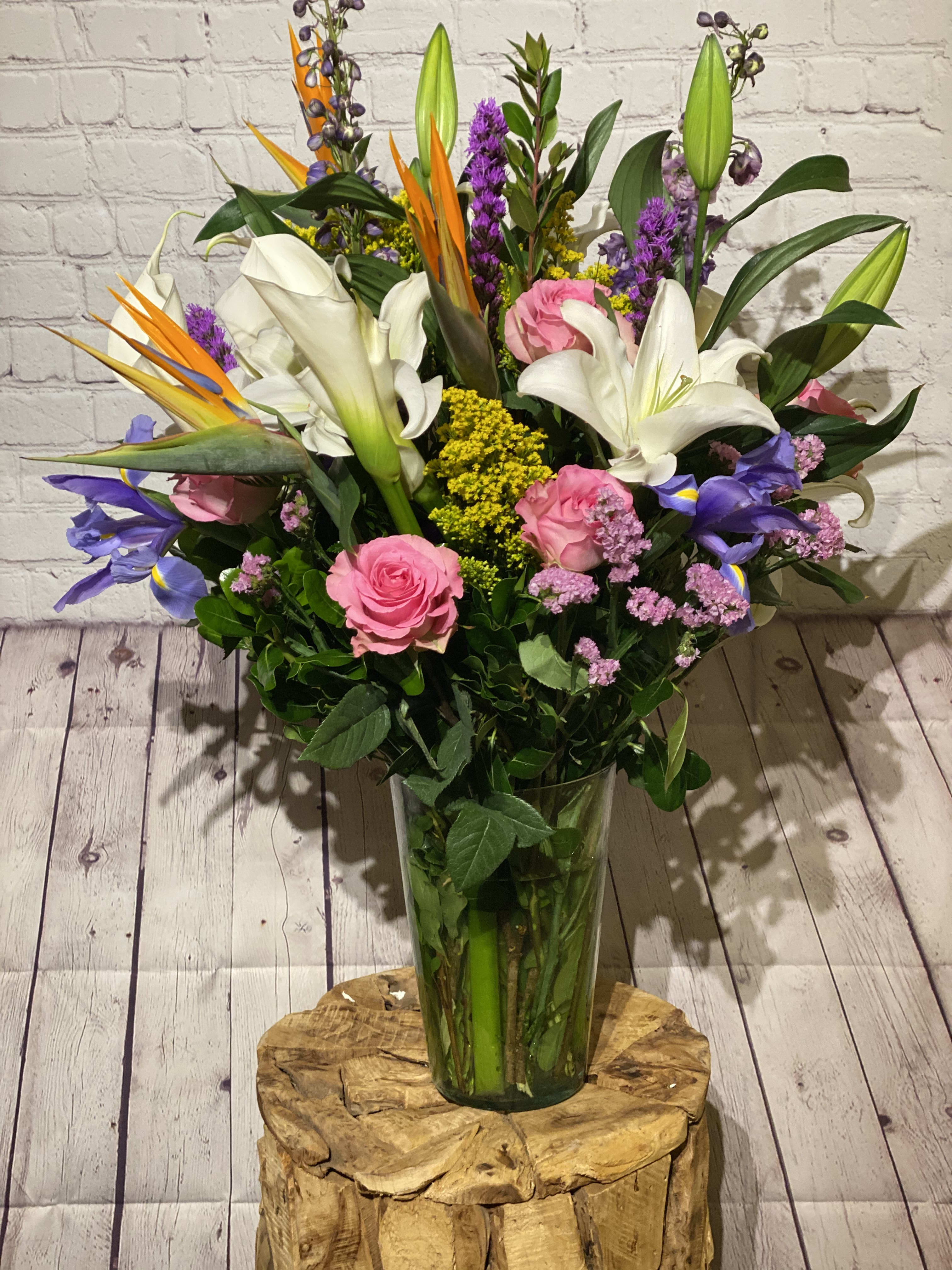 Tall mixed bouquet with white lilies, pink roses, and purple flowers in a glass vase