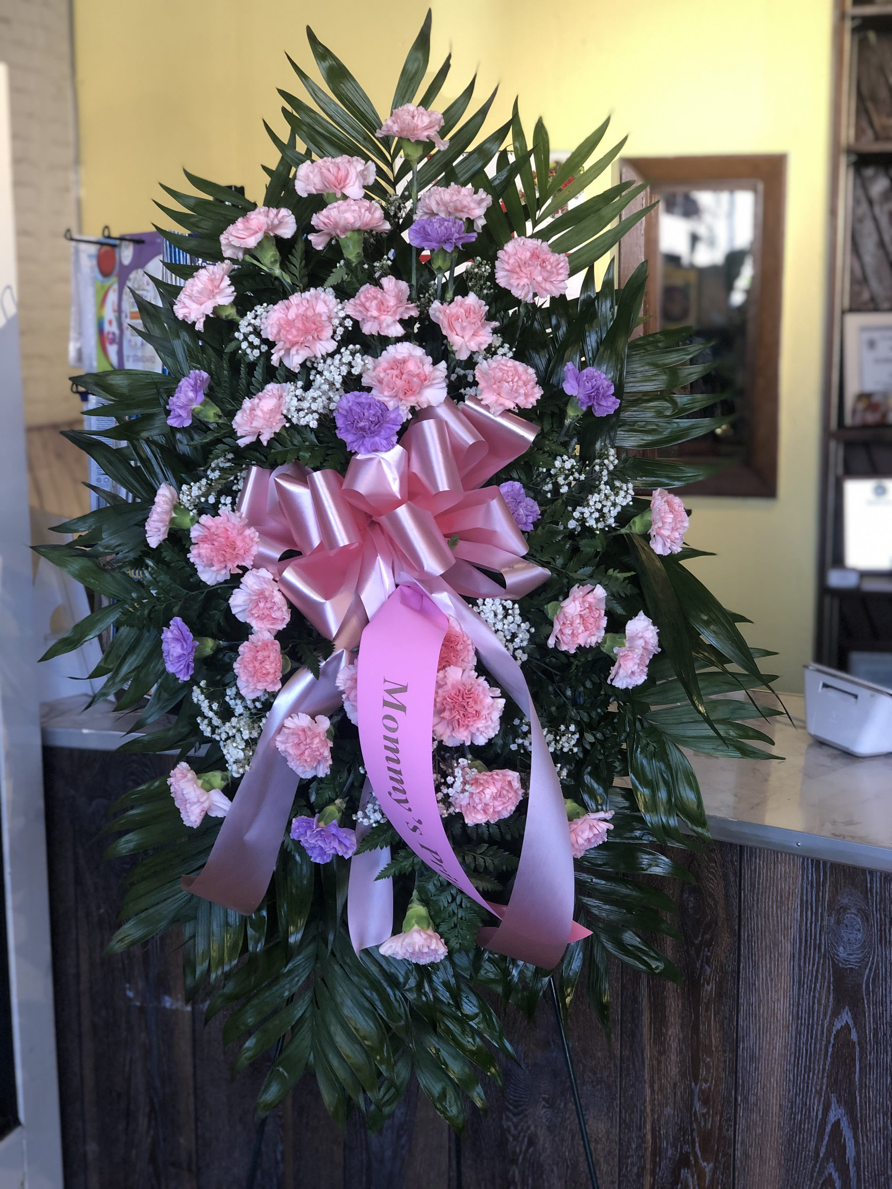 Standing floral spray of pink and purple carnations with a pink ribbon