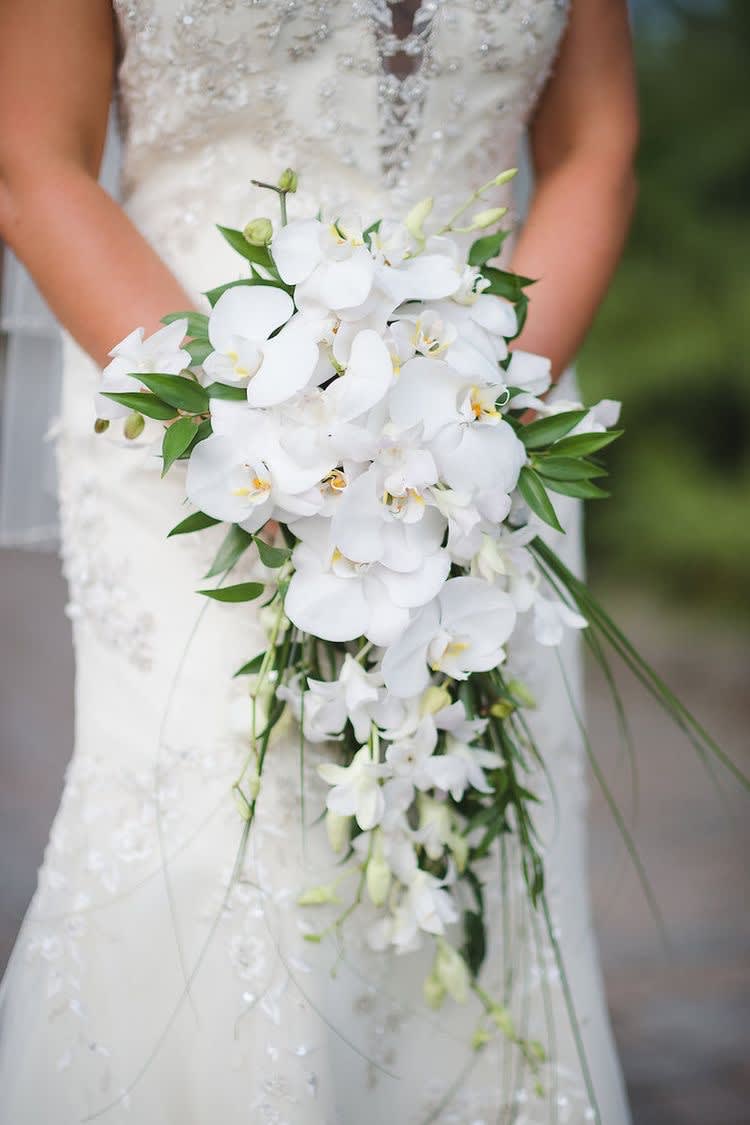 Bride holding a cascading white orchid bouquet with green accents