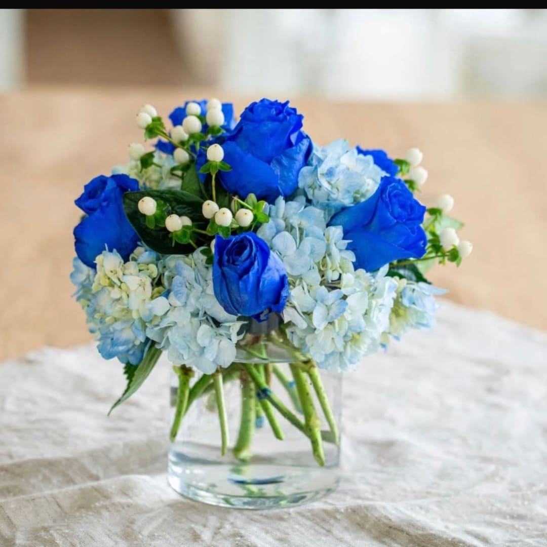Blue roses and pale hydrangeas in a clear glass vase