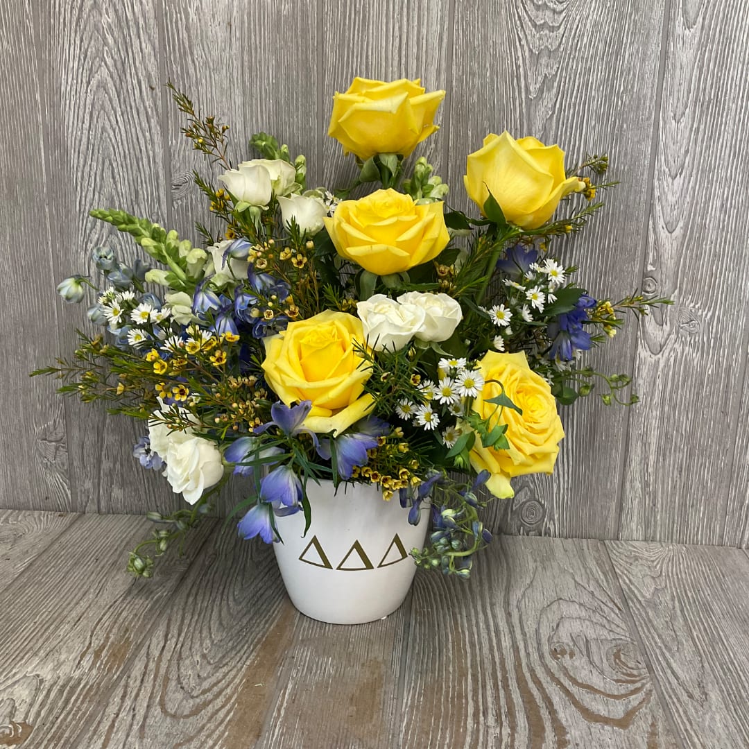Yellow and white roses with blue flowers in a white vase