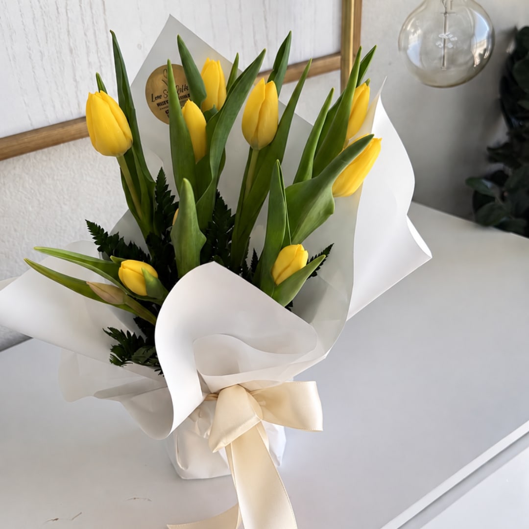 Yellow tulip bouquet wrapped in white paper with a cream ribbon