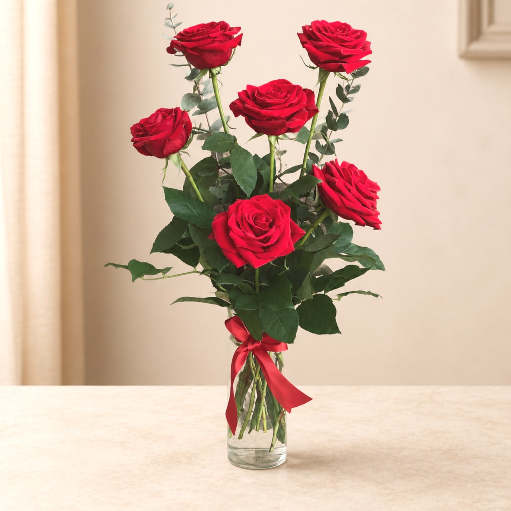 Tall bouquet of red roses in a clear glass vase with a red ribbon