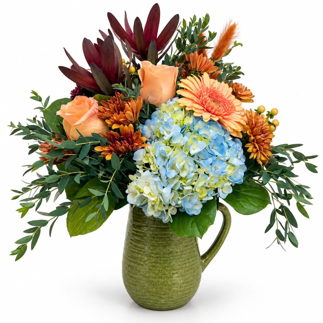 Bouquet of peach roses, blue hydrangeas, and orange mums in a green pitcher