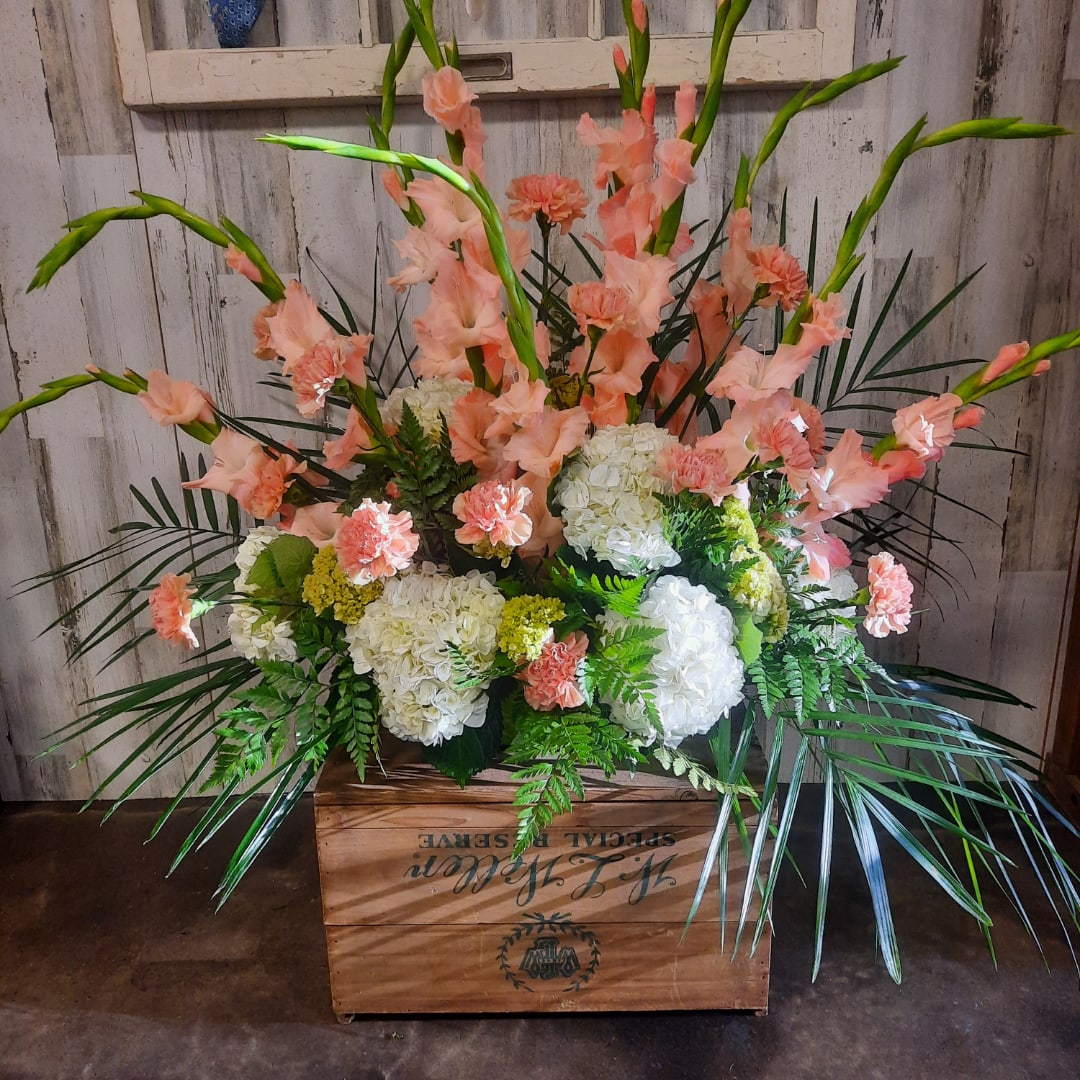 Peach gladiolus and white hydrangeas arranged in a wooden crate