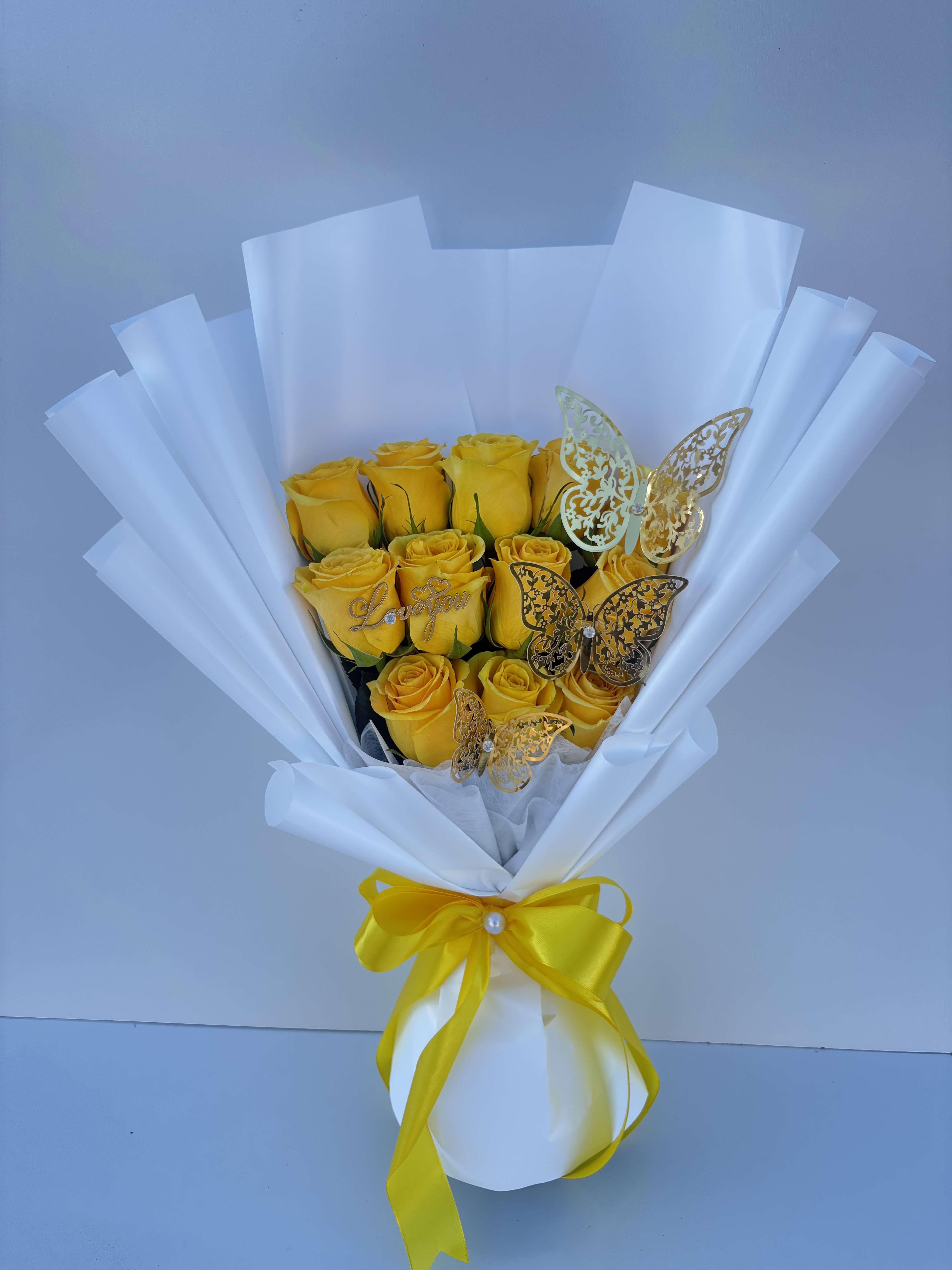 Bouquet of yellow roses wrapped in white paper with a yellow ribbon