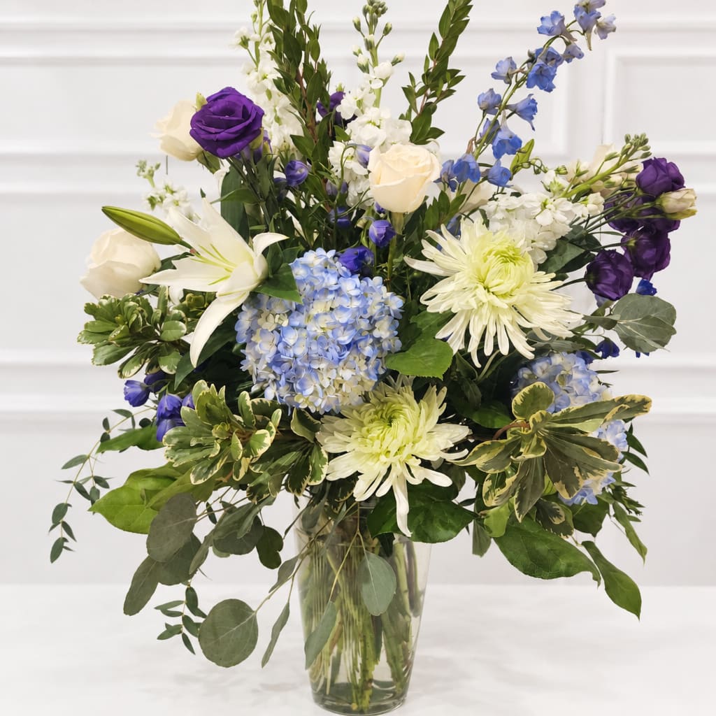 Mixed bouquet of white, blue, and purple flowers in a clear glass vase