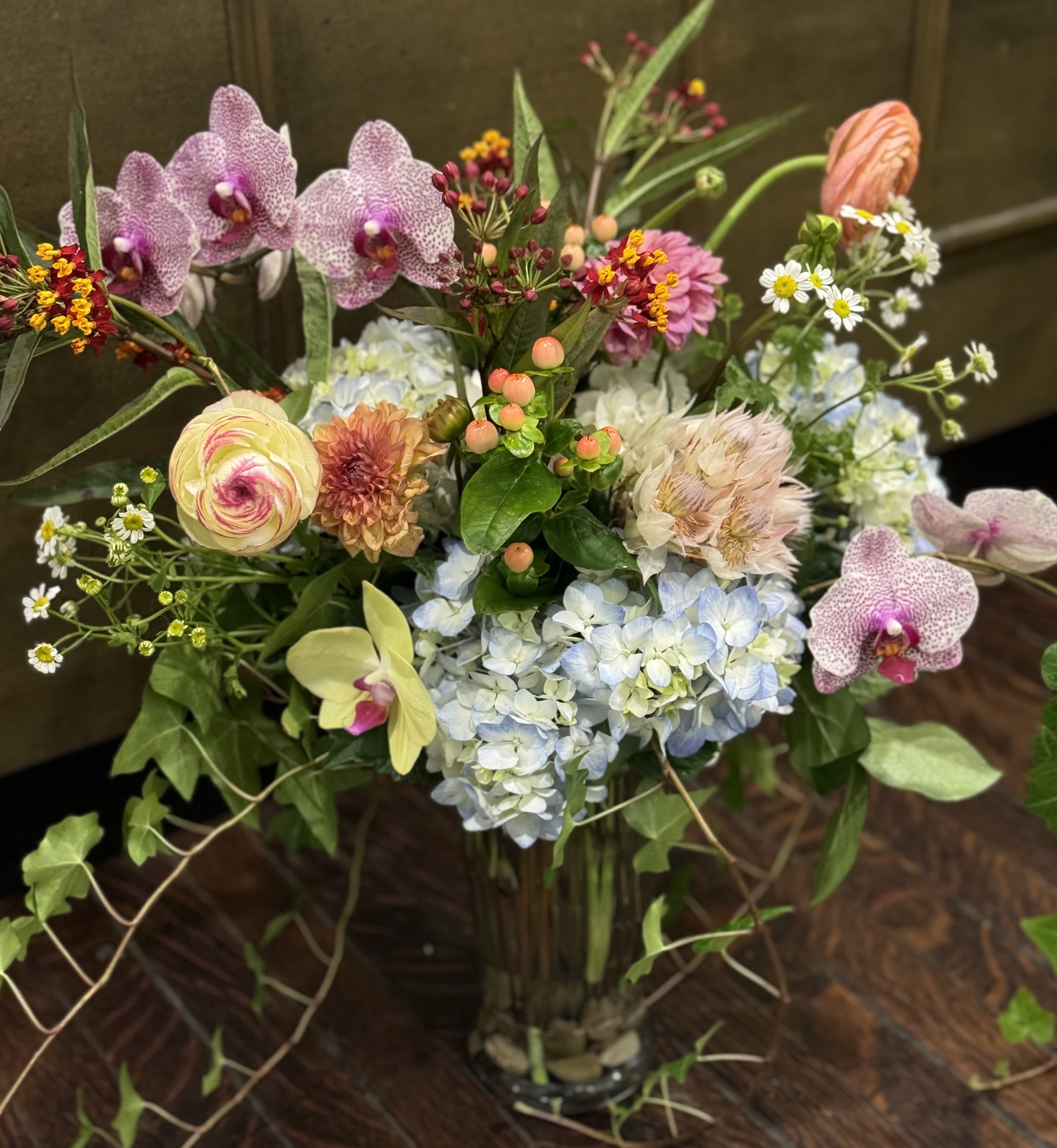 Mixed bouquet with orchids, hydrangeas, and small daisies in a glass vase