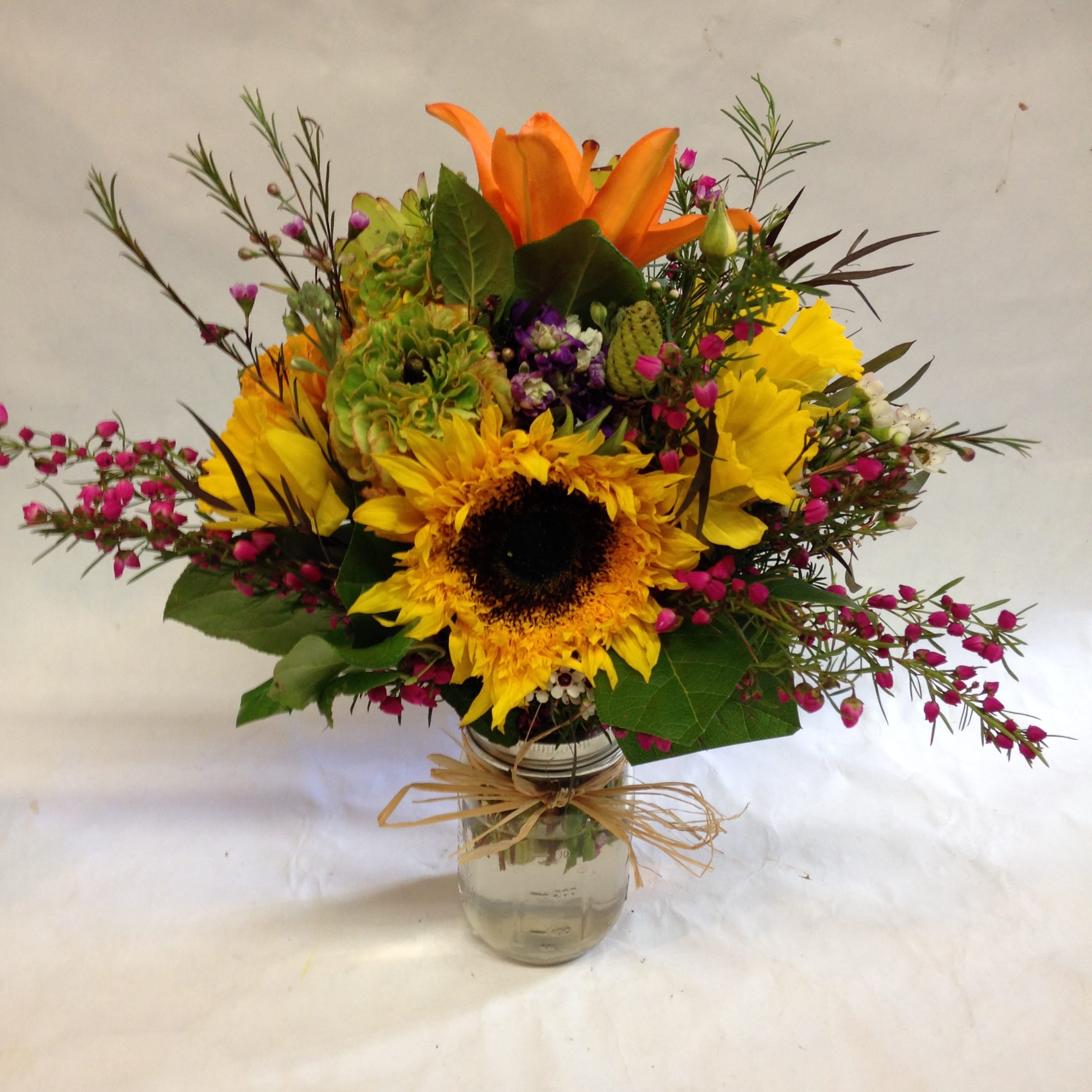 Bright arrangement with a sunflower, orange lily, and mixed blooms in a mason jar vase