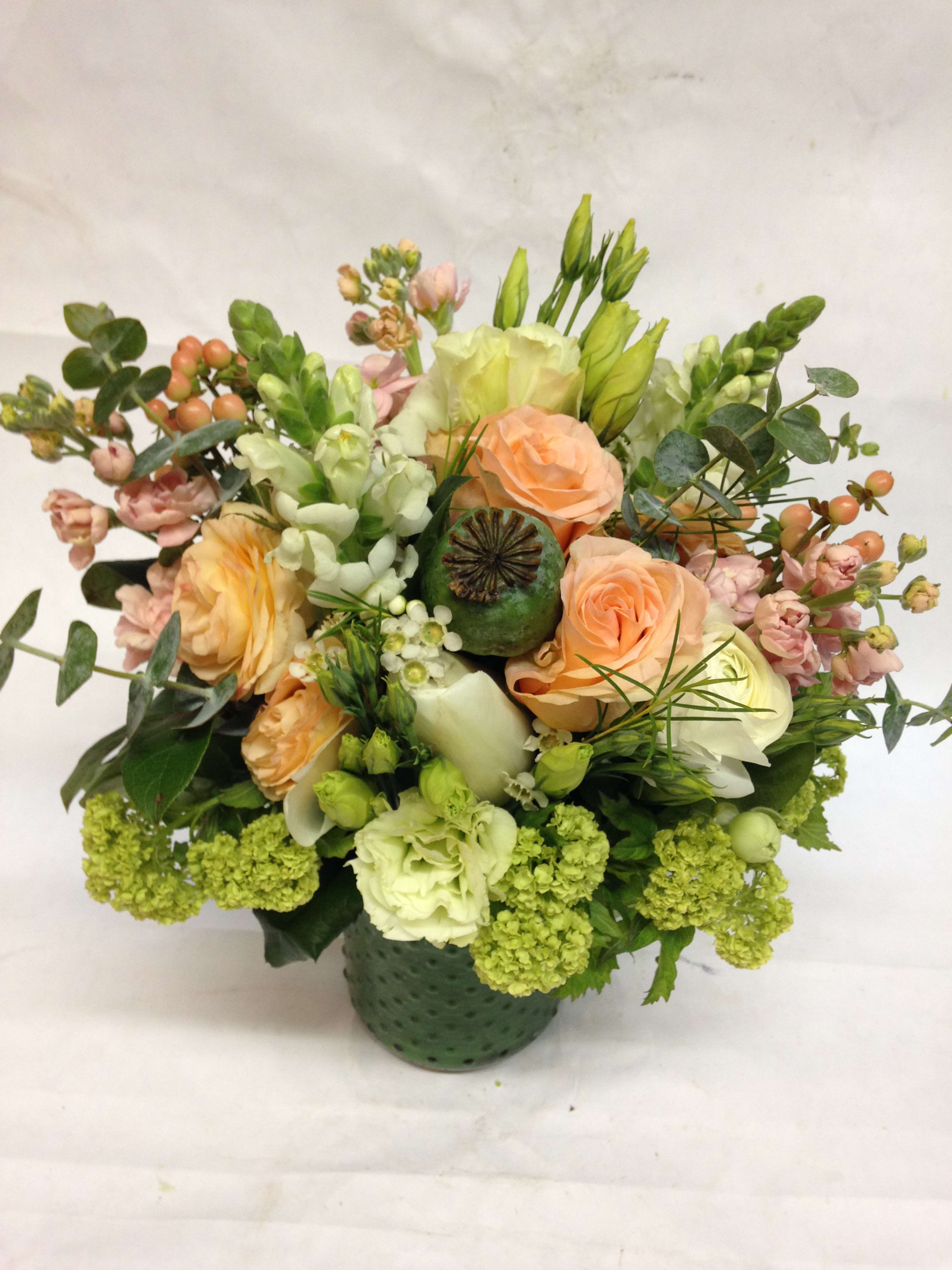 Mixed bouquet of peach roses, white blooms, and green flowers in a green vase