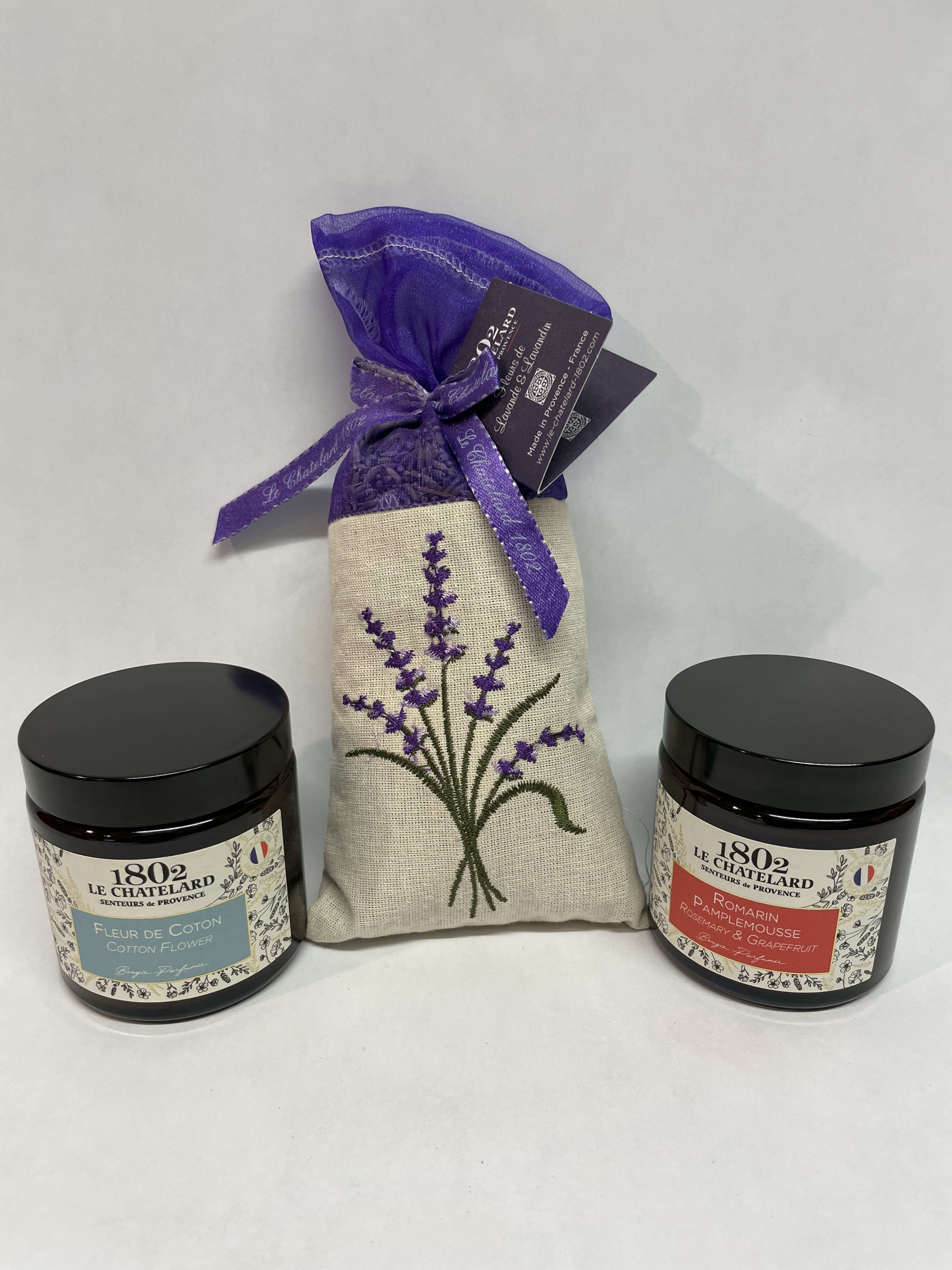 Two scented candles flank a lavender sachet gift bag.