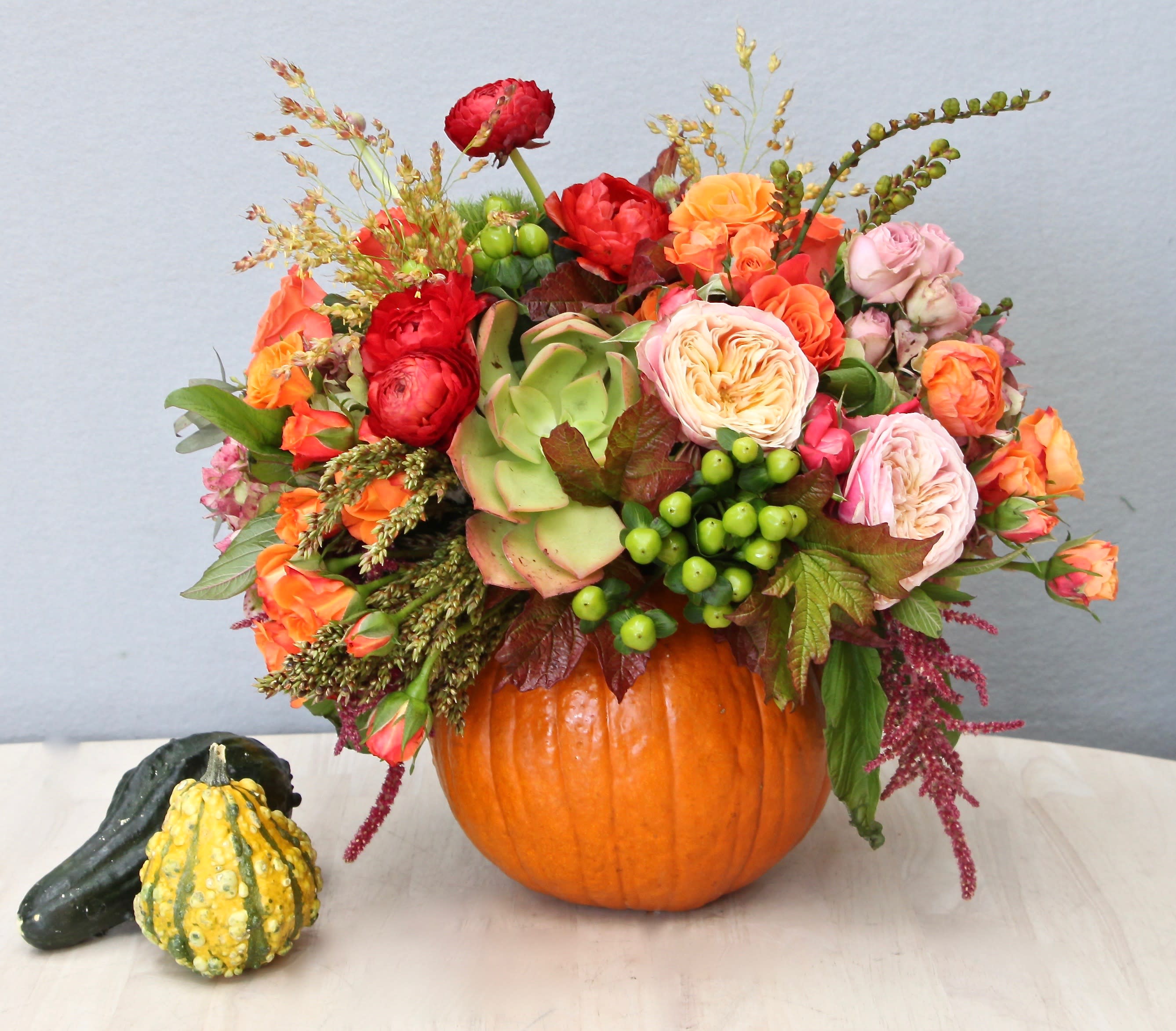 Autumn flower arrangement in a hollow pumpkin with orange and pink blooms, green succulent, and berries