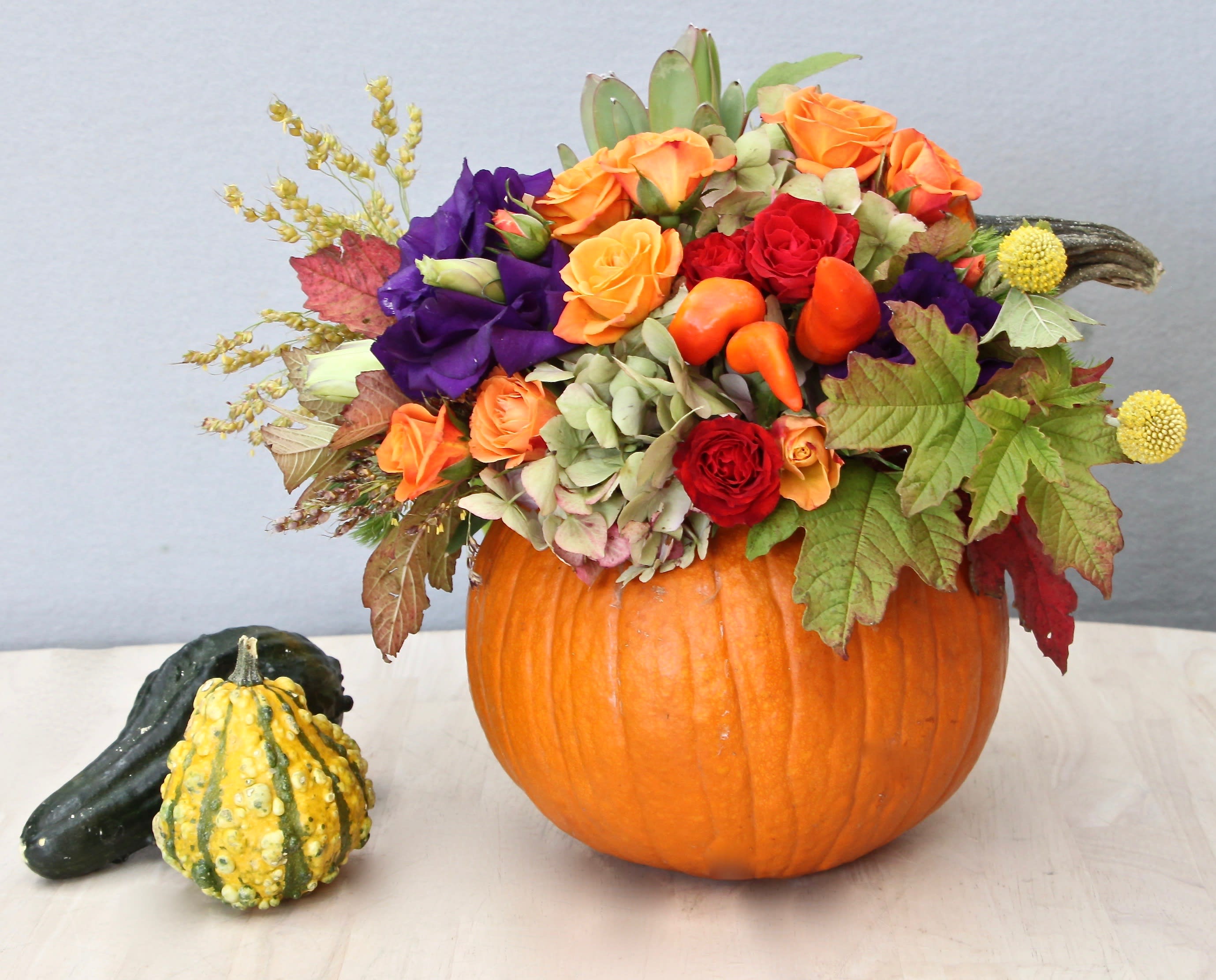 Autumn flower arrangement with roses and lisianthus in a hollow pumpkin with decorative gourds