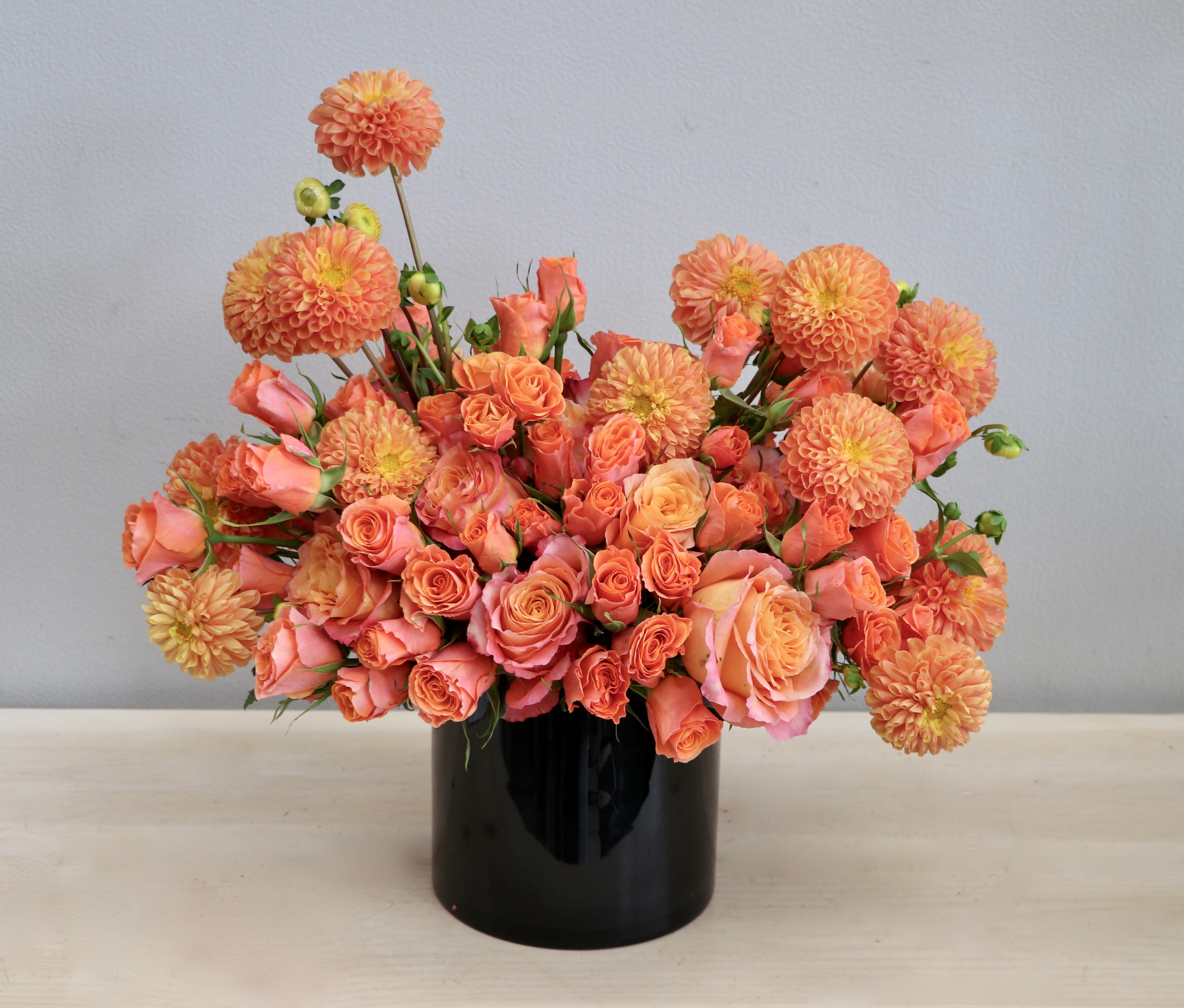 Low orange and peach rose and dahlia arrangement in a black cylinder vase