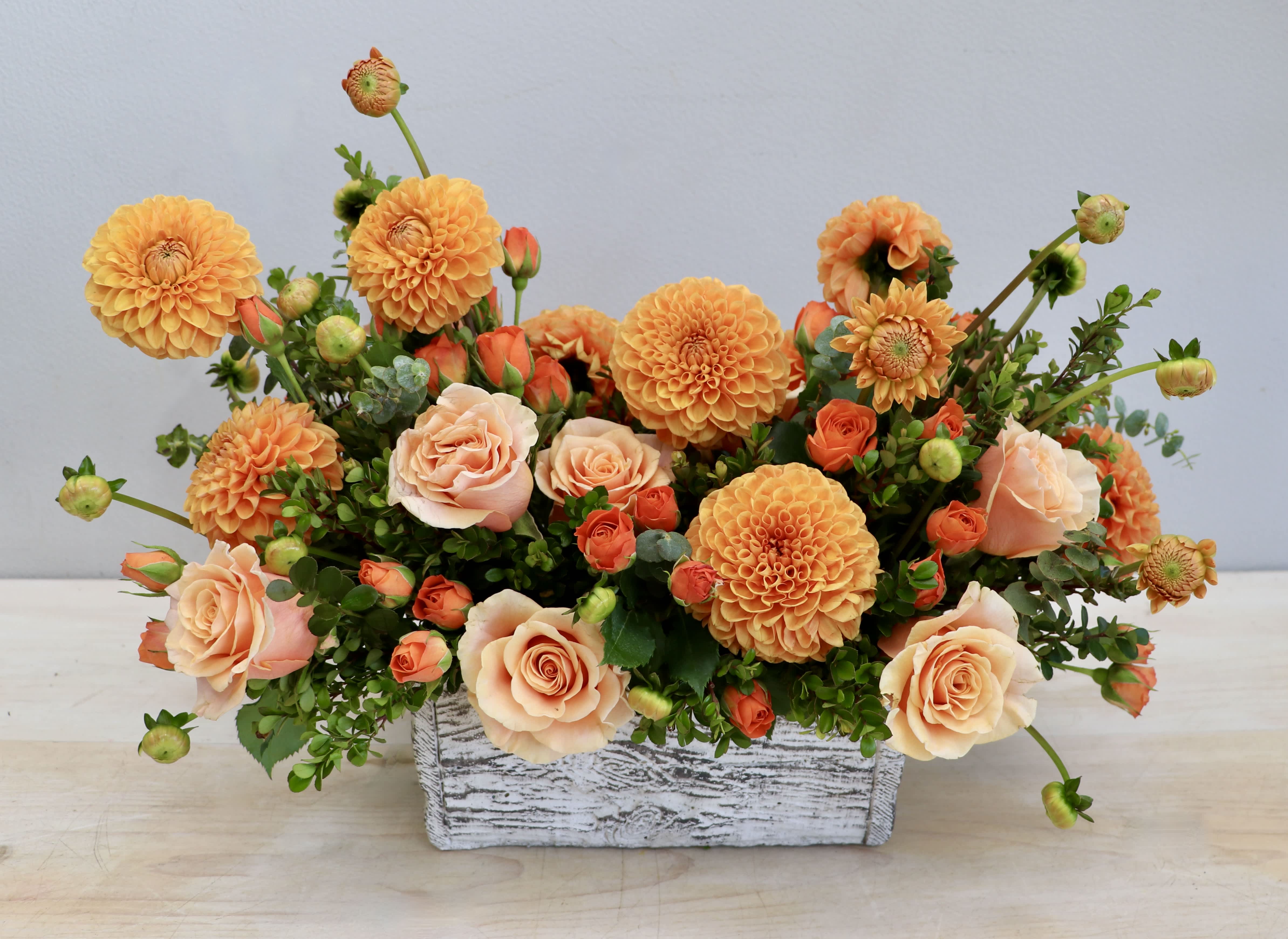 Low arrangement of orange dahlias and peach roses in a whitewashed wooden box