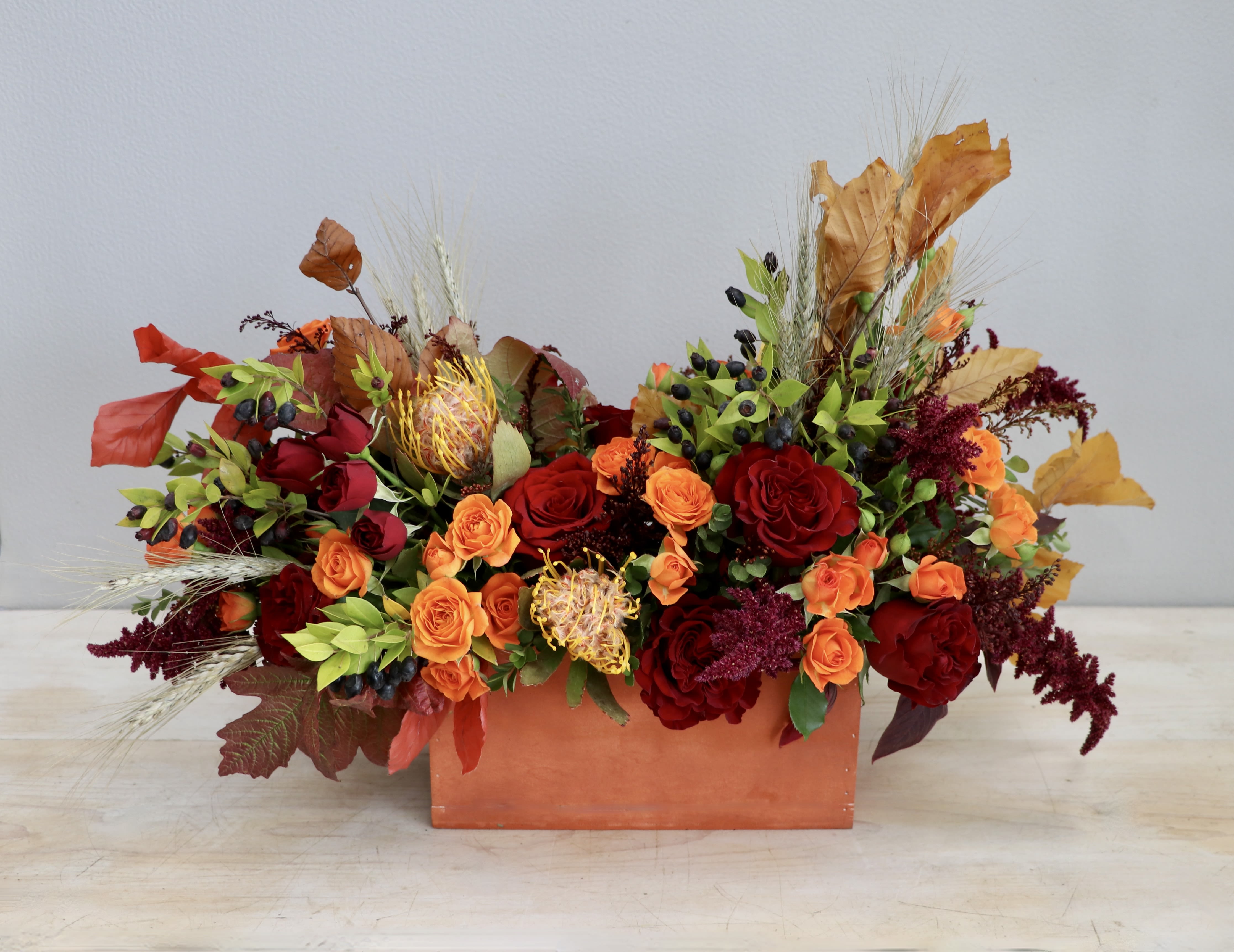 Low rectangular arrangement of red and orange roses with pincushion protea in an orange container