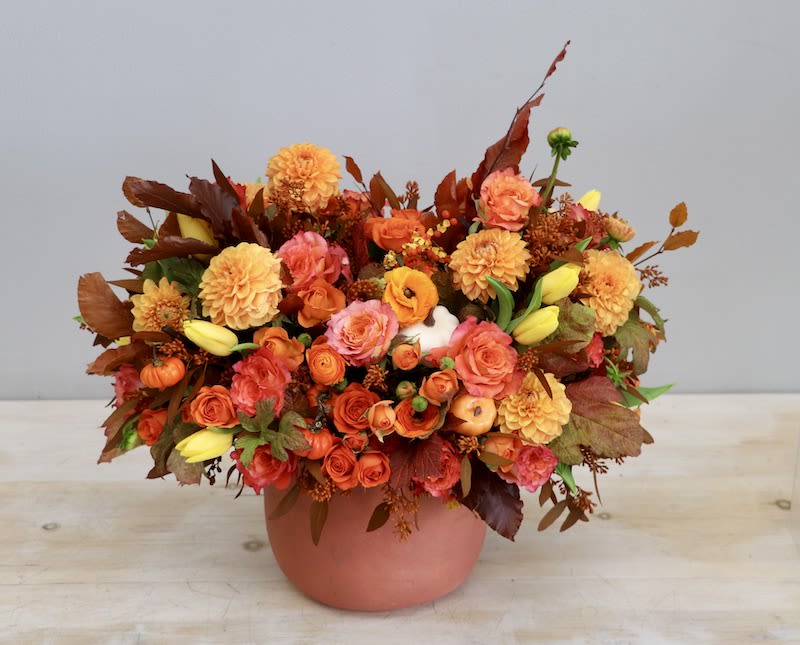 Low orange and yellow autumn flower arrangement with roses and dahlias in a terracotta pot.