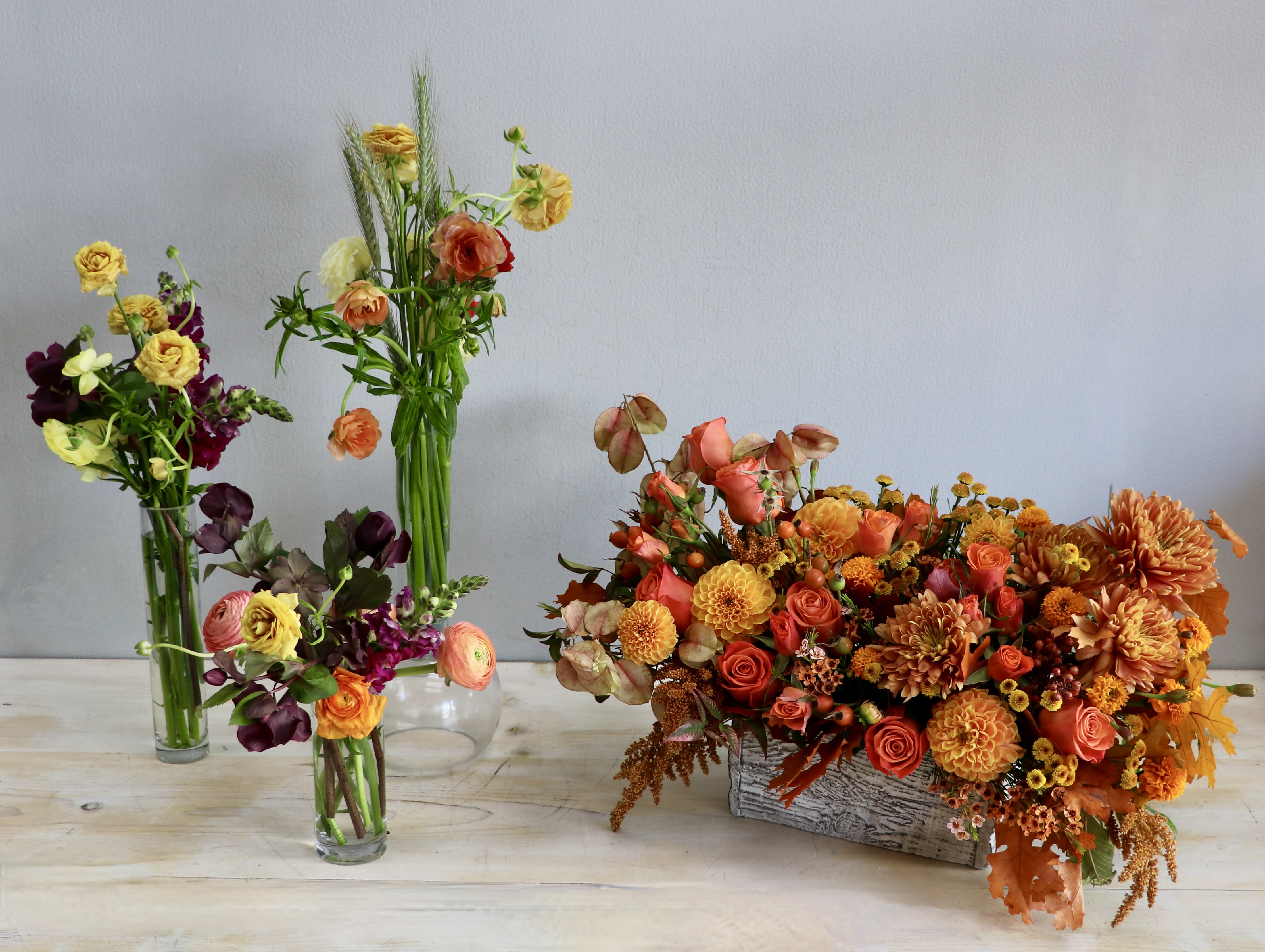 Set of orange and yellow mixed flower arrangements in glass vases and a rustic rectangular container