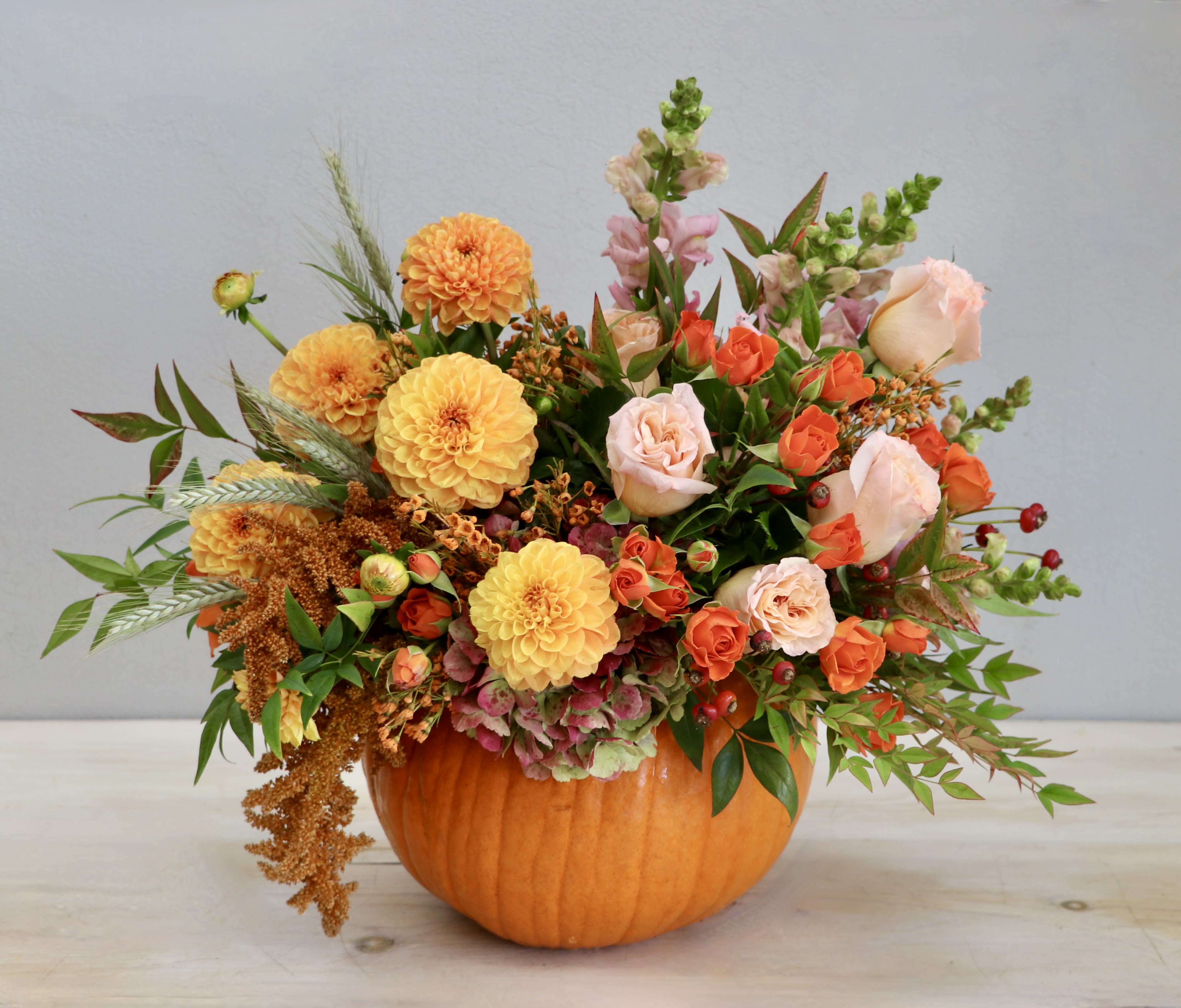 Autumn arrangement of orange and peach flowers in a hollow pumpkin container