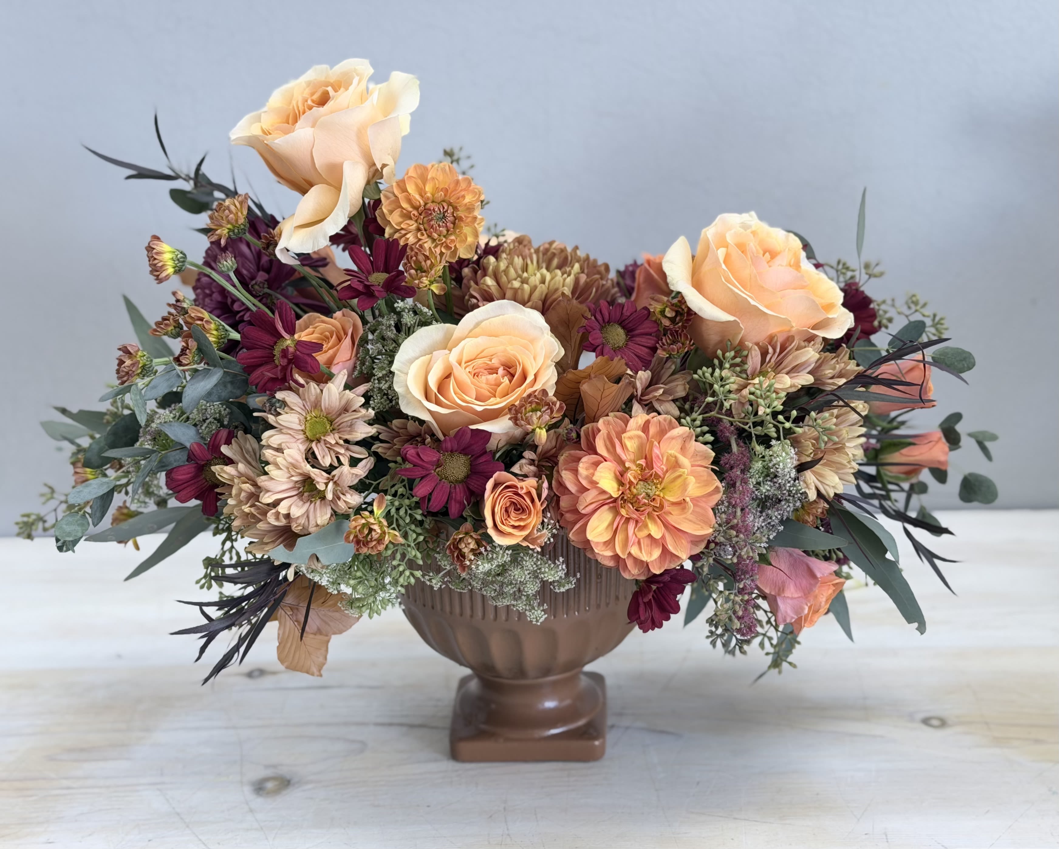 Low centerpiece of peach roses and mixed autumn flowers in a brown pedestal bowl